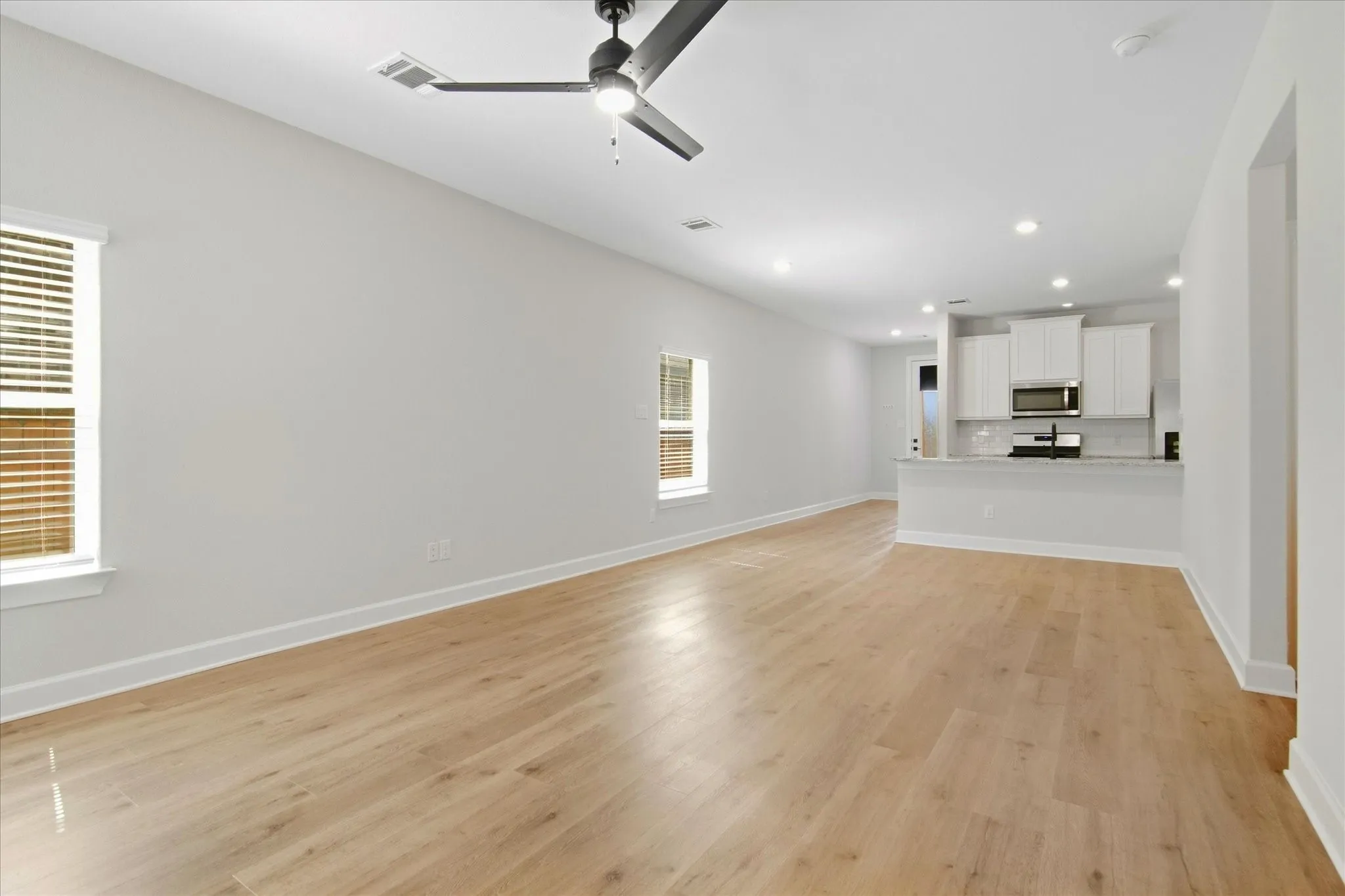 Light wood-finish flooring, white walls, and a contemporary ceiling fan