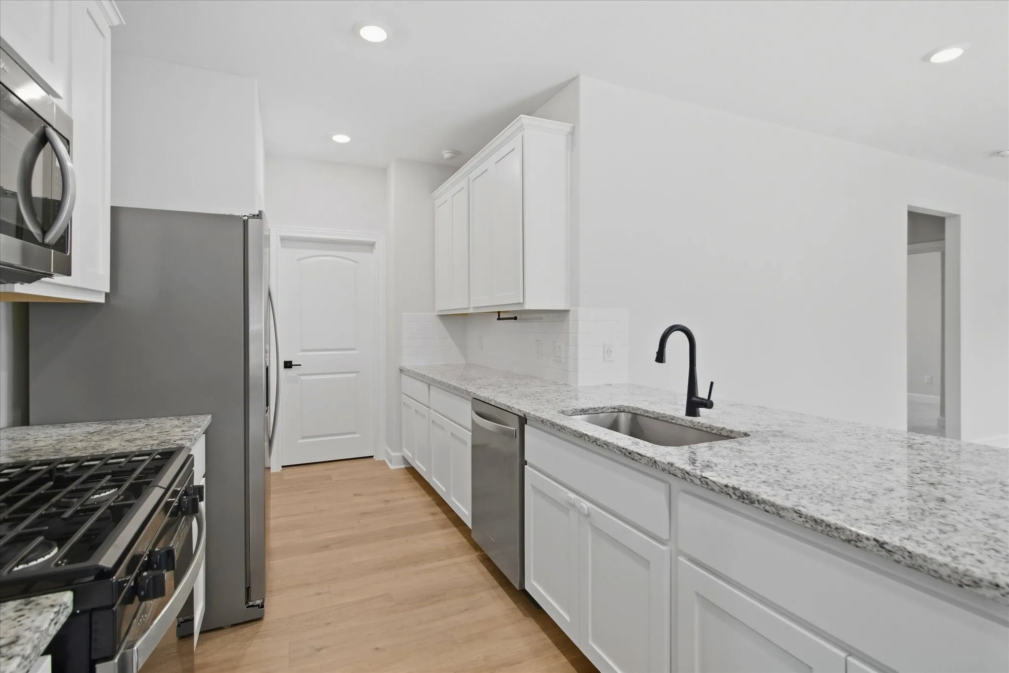 Full kitchen featuring stainless steel appliances, white cabinetry, light wood-finish flooring, and light-toned countertops