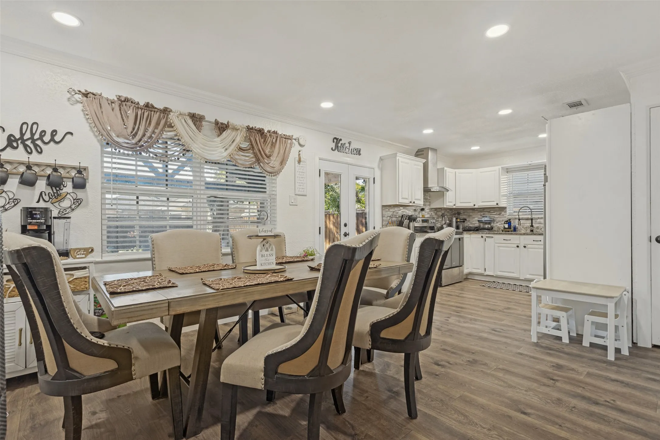 Open-concept area featuring wood-finish flooring, recessed lighting, white cabinetry, a built-in kitchen range hood, and glass-paneled double doors