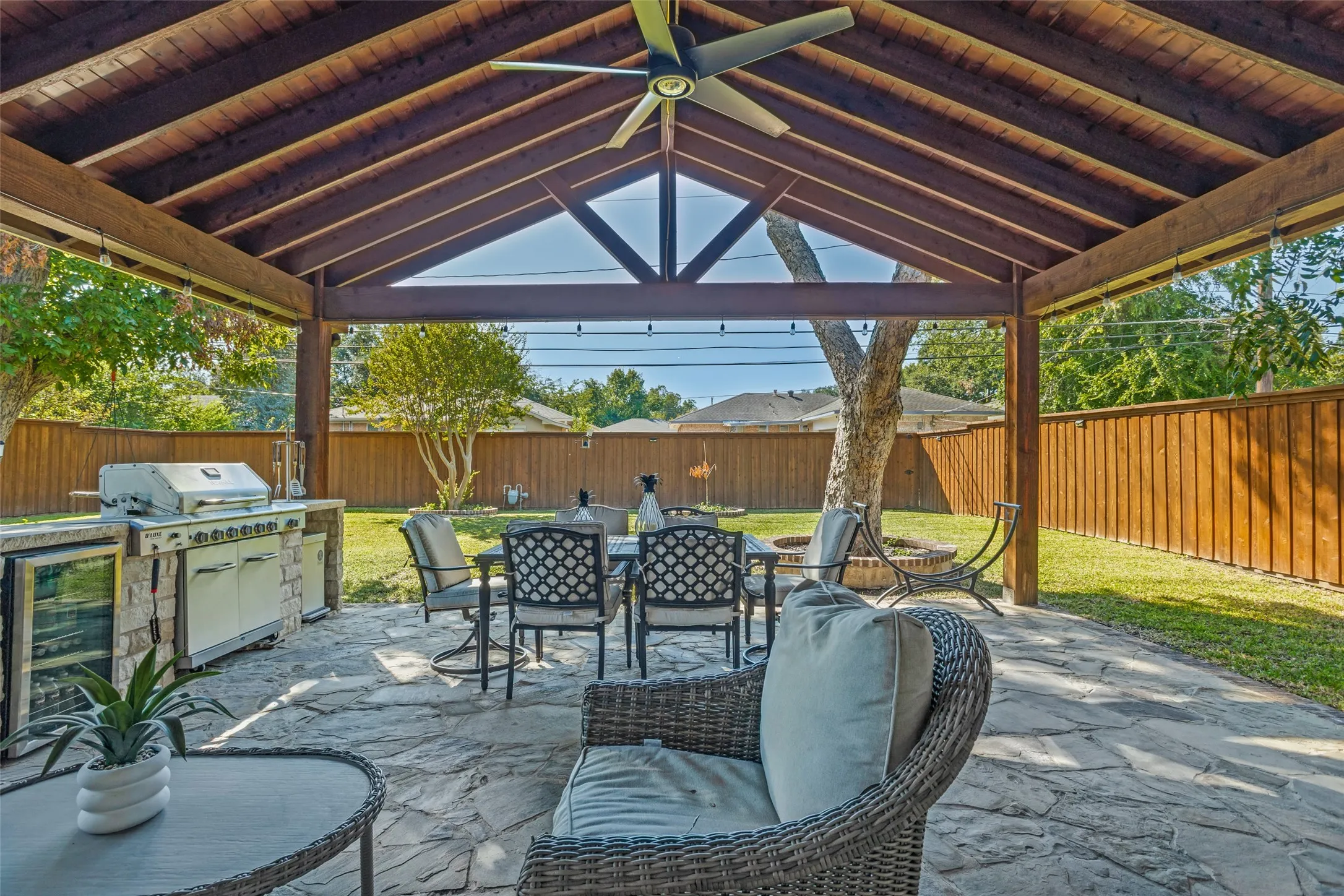 Covered patio featuring an exposed timber-beam ceiling, stone-paved flooring, built-in outdoor kitchen with stone base, and a dedicated ceiling fan