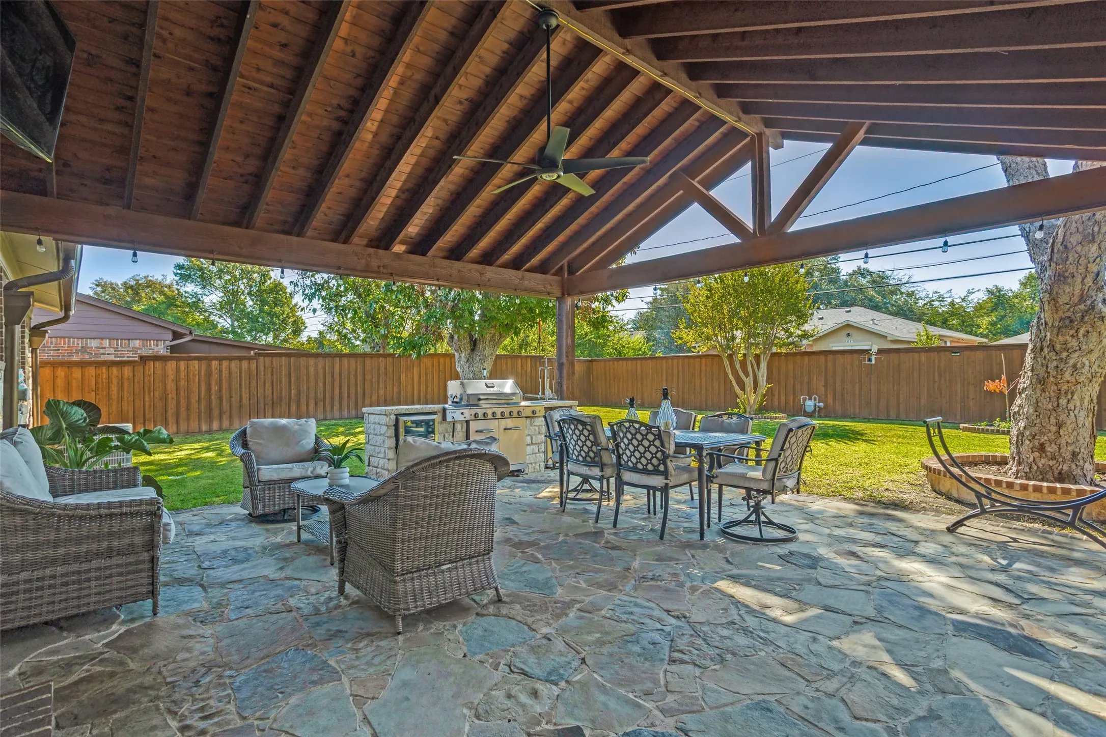 Covered outdoor living space featuring a timber-framed vaulted ceiling, flagstone patio, built-in masonry grill station, and integrated ceiling fan