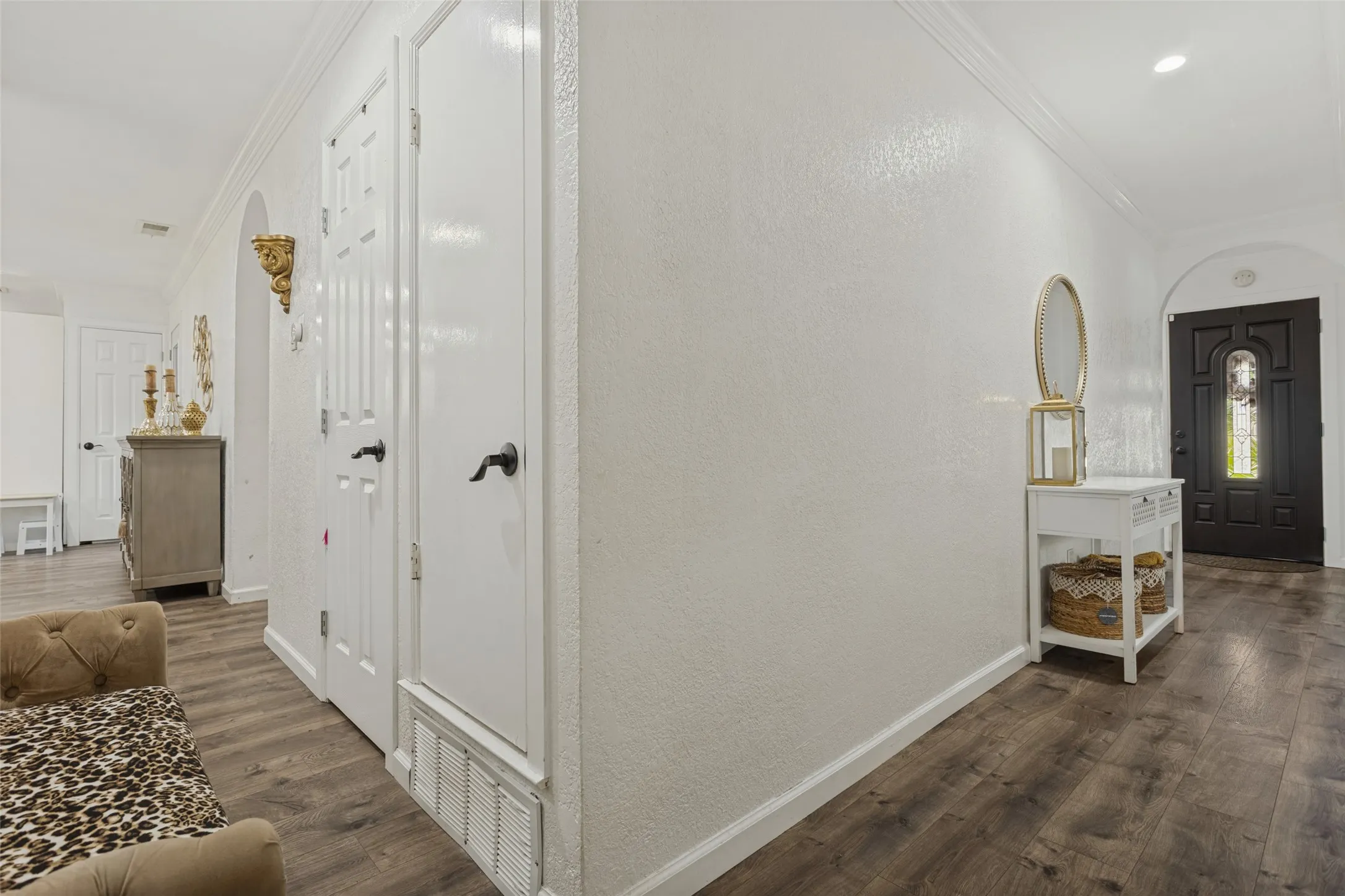 Entryway featuring dark-stained wood-finish flooring, white paneled doors with matte black hardware, arched wall openings, and a dark-finished exterior entry door with an integrated glass panel
