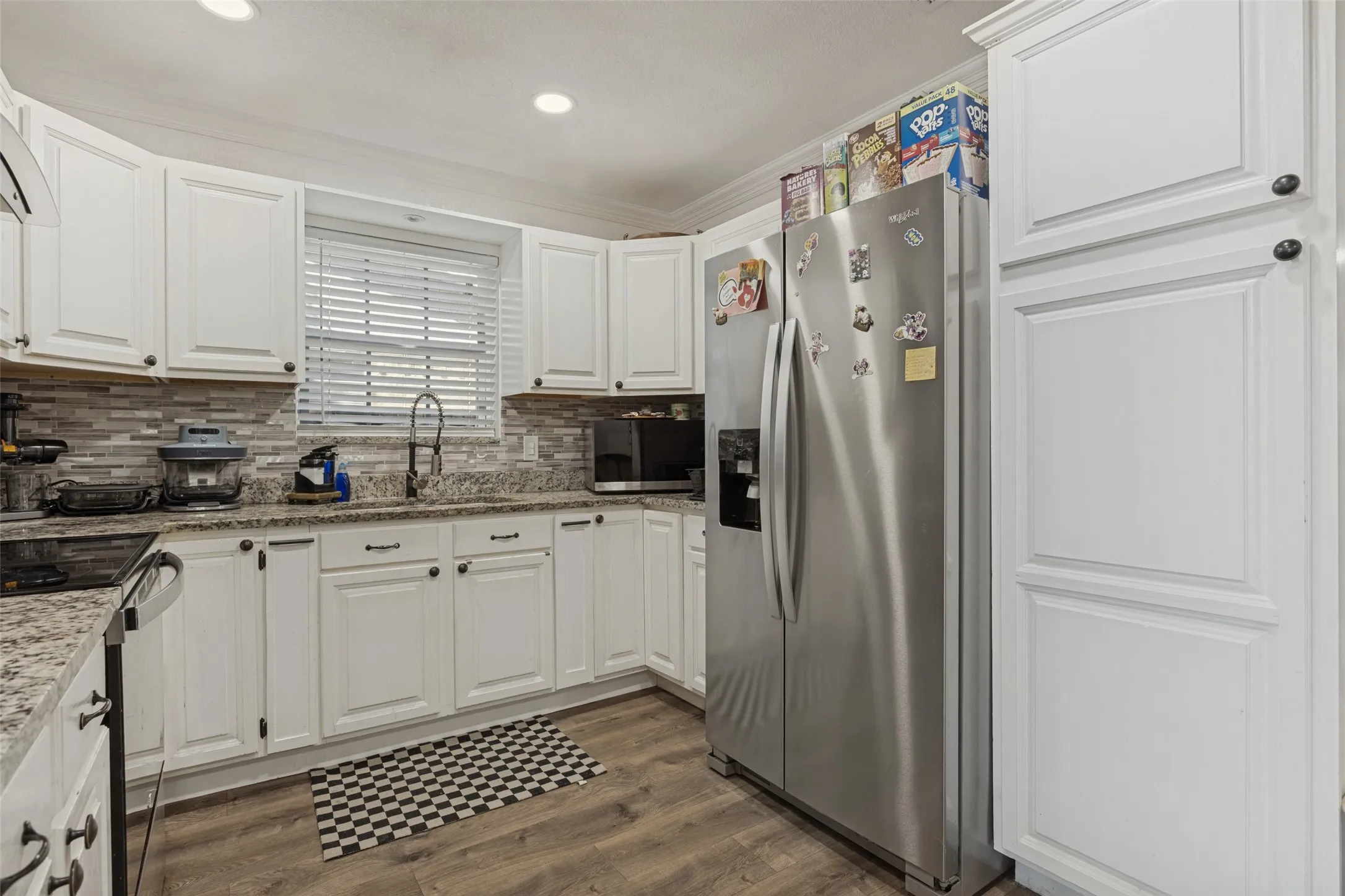 Kitchen featuring white cabinetry, stone-surface countertops, stone tile backsplash, wood-finish flooring, and recessed lighting