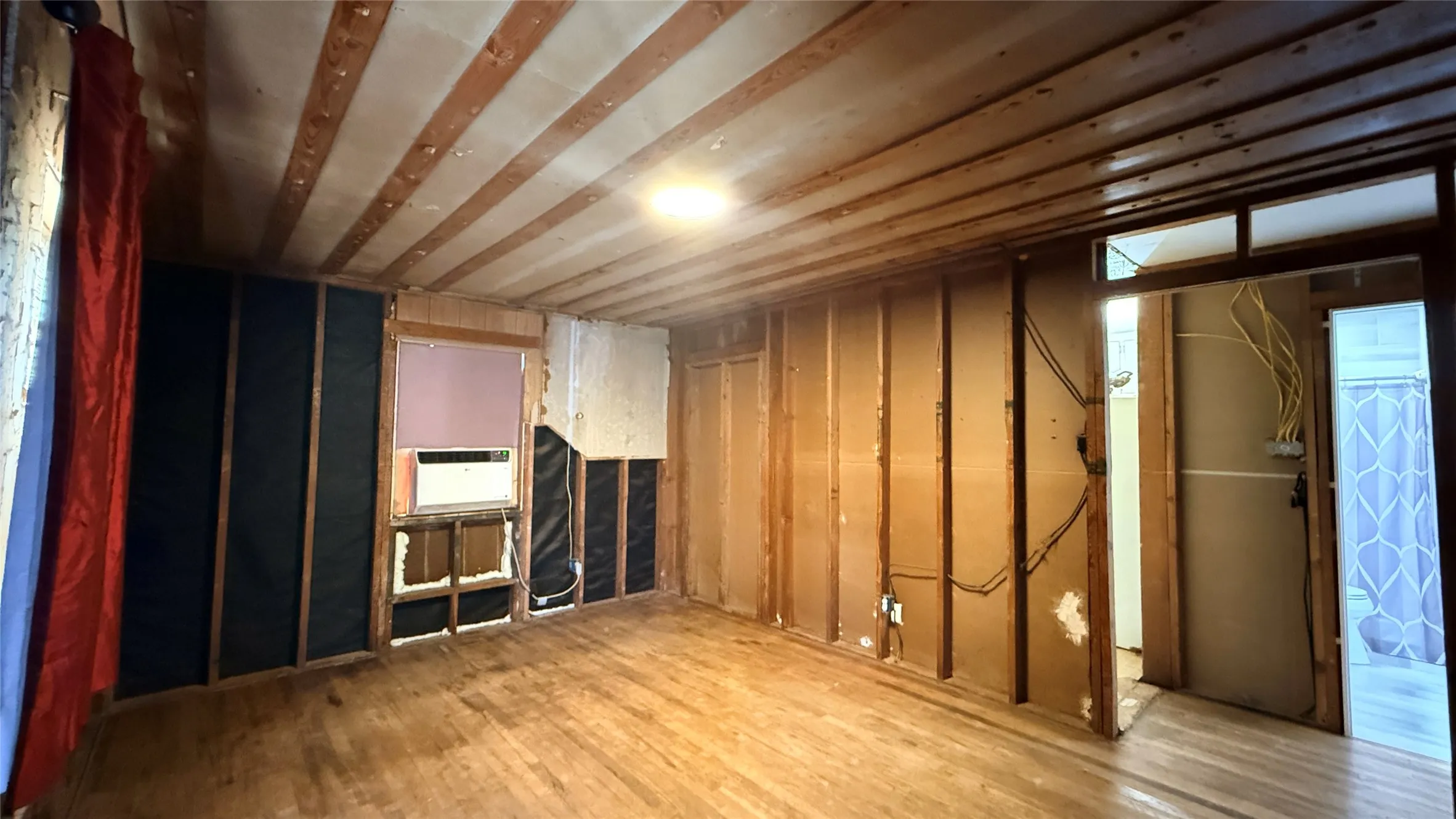 Hardwood flooring, wood-paneled ceiling, exposed wall studs, and window opening