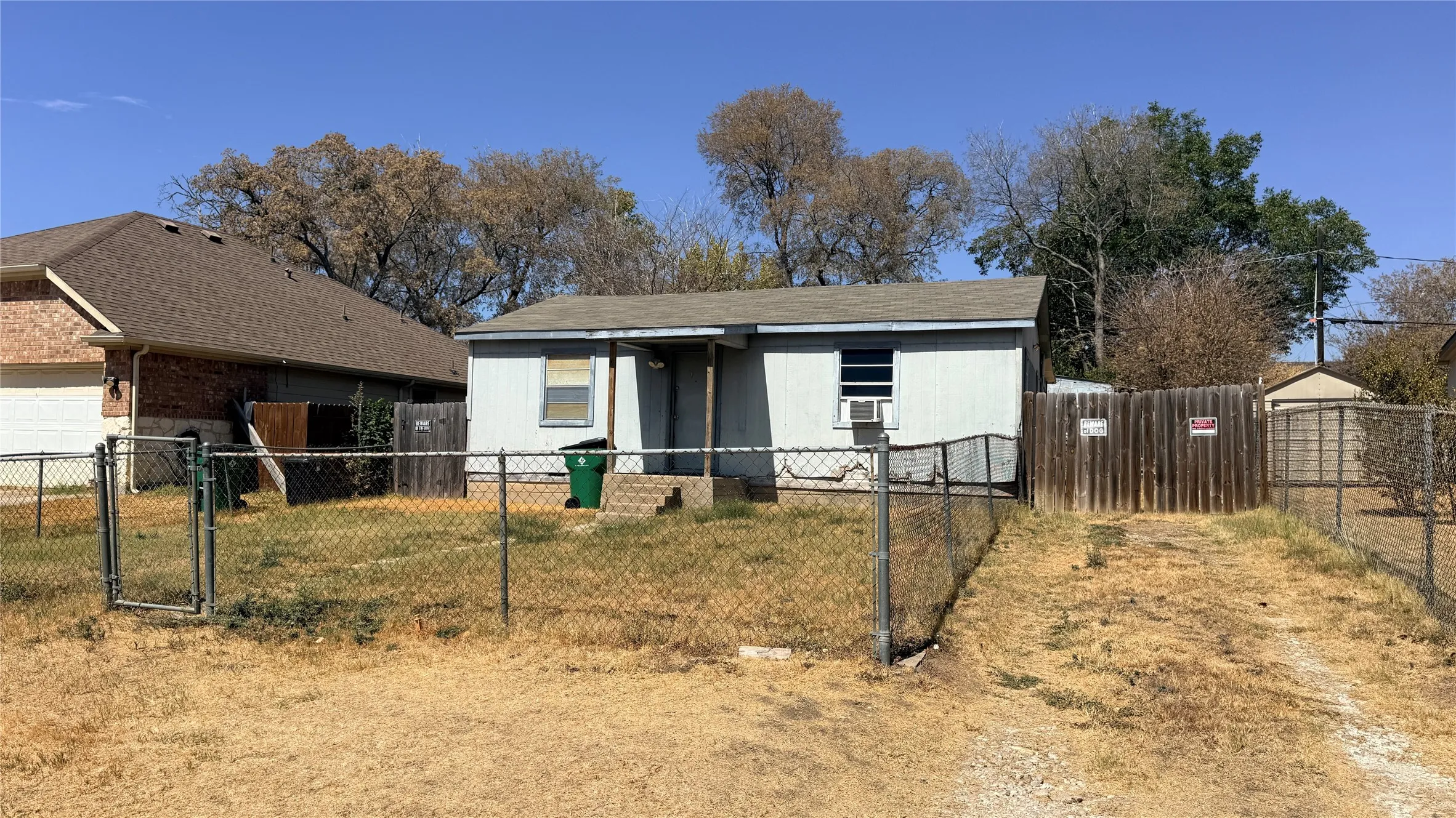 Chain link fence encompassing the property, gravel driveway, and a wood privacy fence