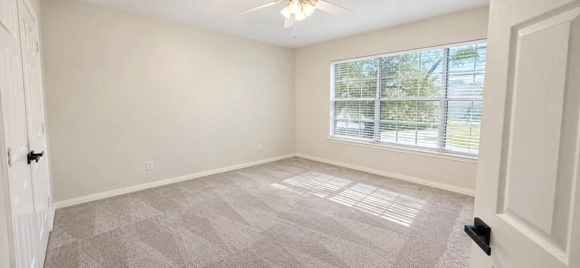 Neutral paint palette, textured carpet, ceiling fan, and large window with blinds