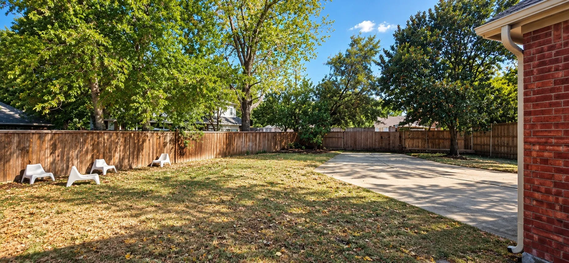 Expansive lawn area, concrete pad, wood privacy fencing, mature trees, and brick exterior