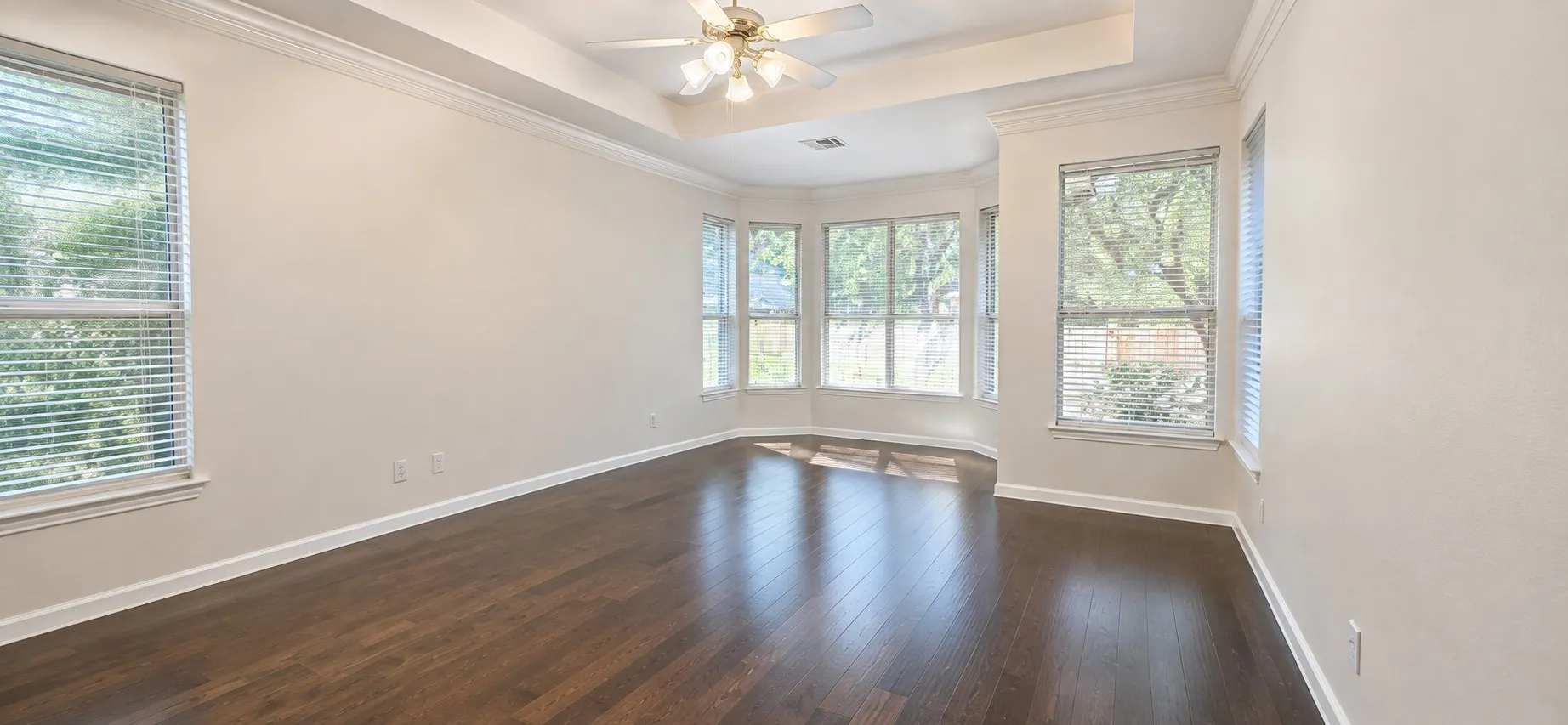 Tray ceiling with a ceiling fan, wood-finish flooring, and bay windows