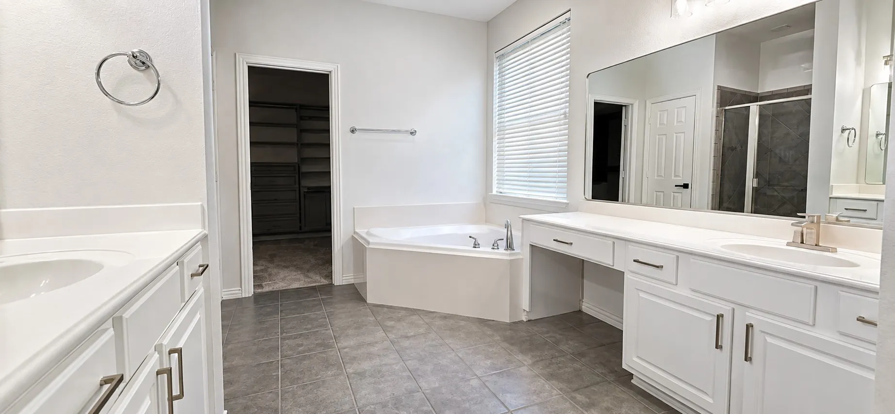 Dual vanity with white cabinetry, built-in soaking tub, tiled flooring, and a walk-in closet with shelving