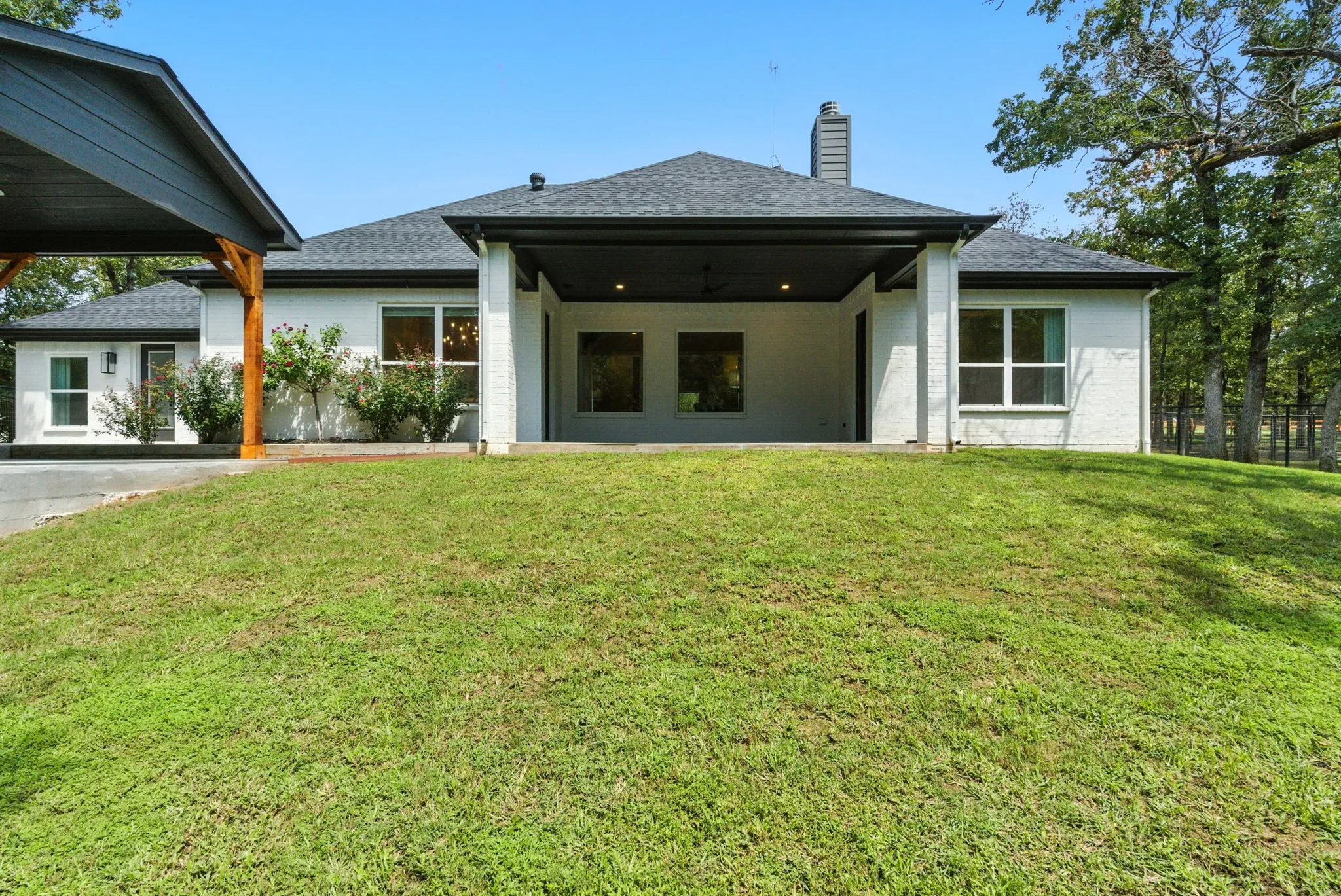 White brick exterior with dark trim, covered patio, and attached carport with wood-finish supports