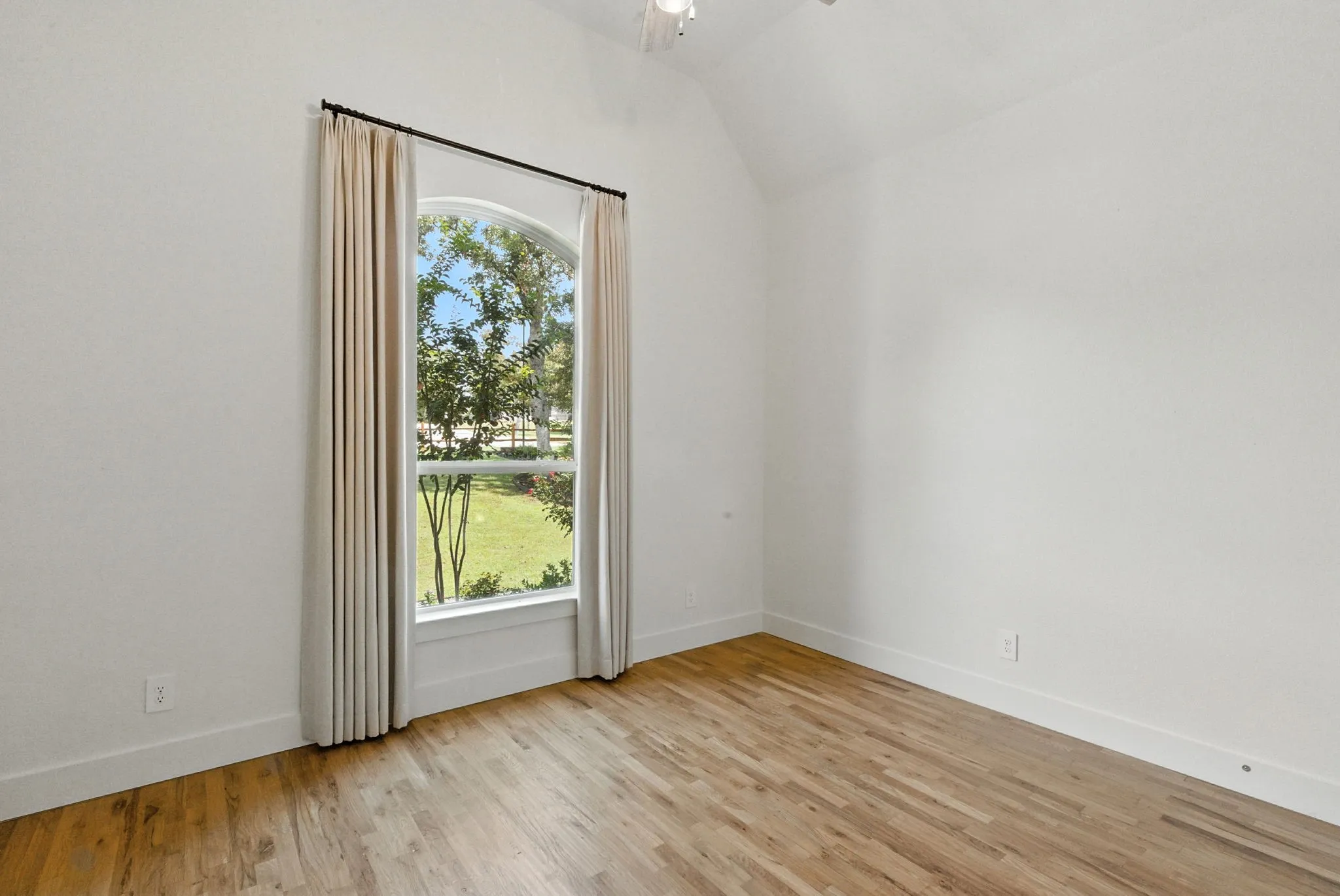 Arched window with exterior landscaping, vaulted ceiling, and wood-finish flooring