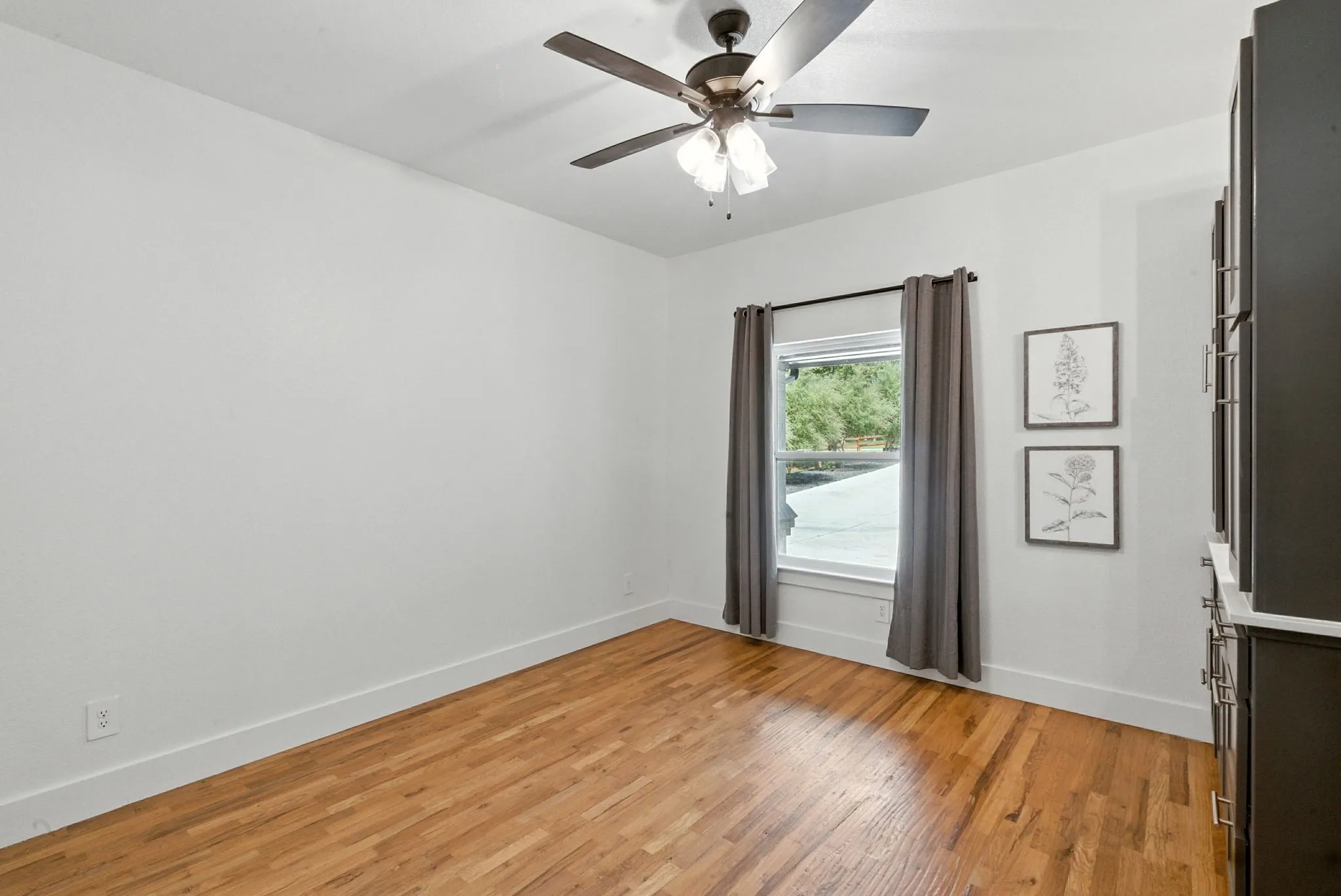 Hardwood flooring, white painted walls, window with trim, ceiling fan light fixture, and built-in cabinetry