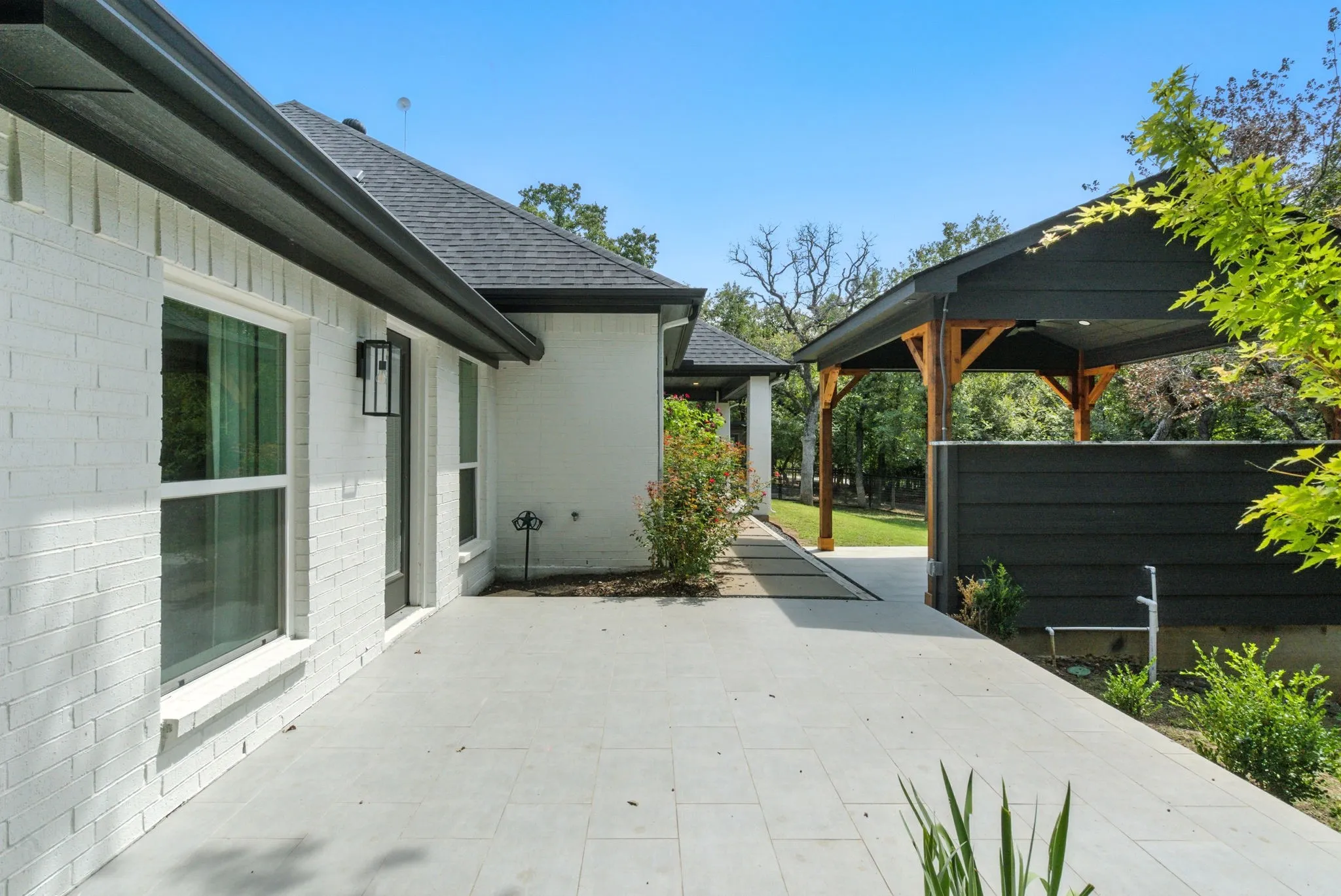 White brick exterior with black trim, concrete patio, and a covered outdoor structure featuring wood beams