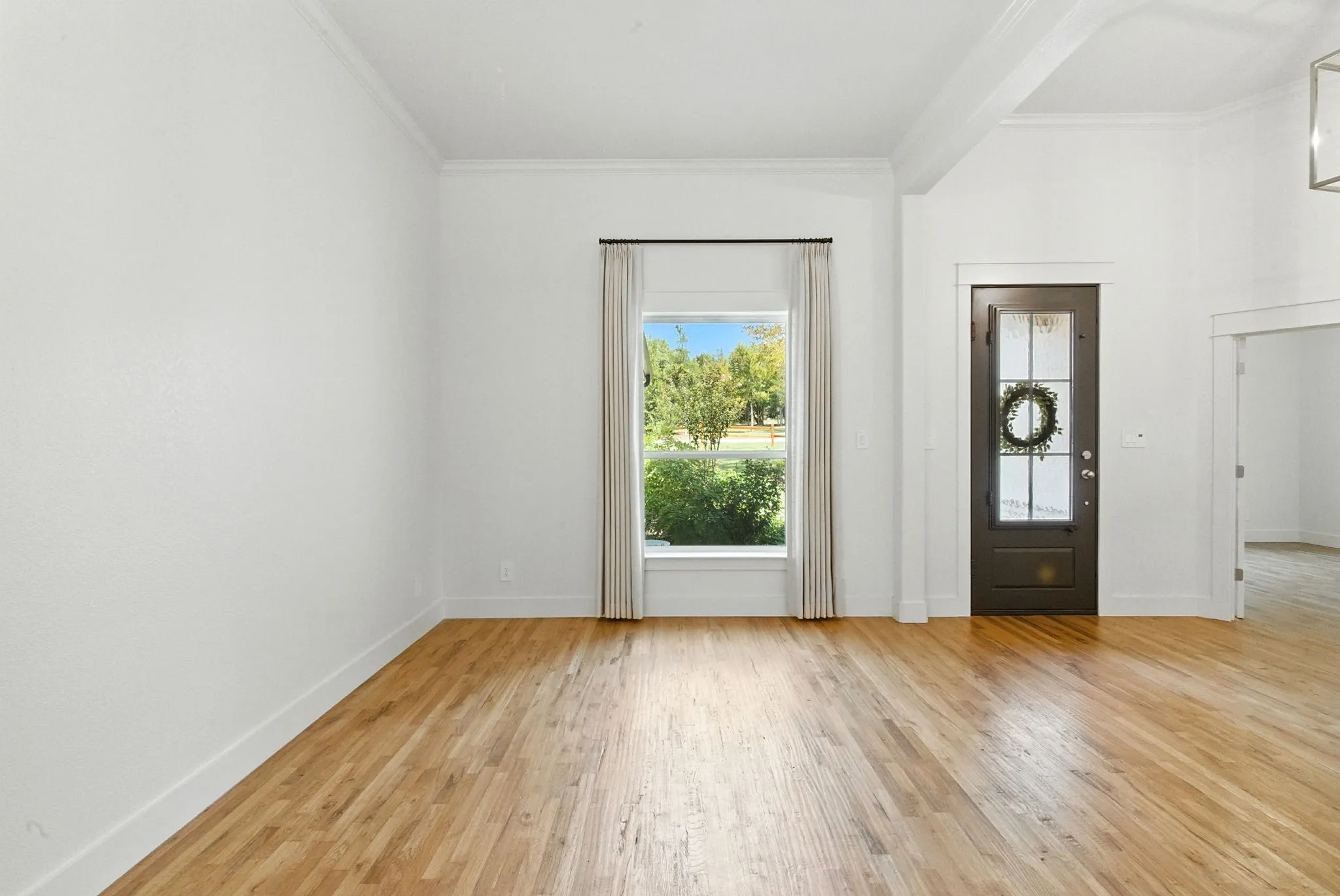 Hardwood flooring, white walls, crown molding, large window, and dark paneled door with glass inserts