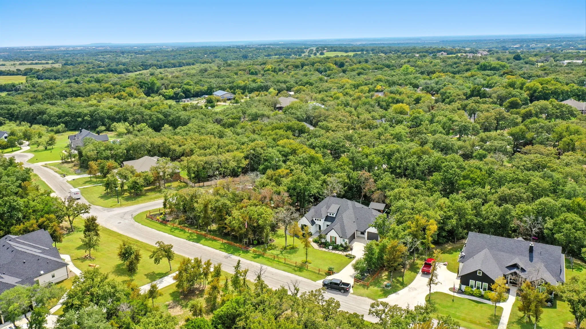 Expansive residential setting featuring mature trees, paved roads, and houses with dark-toned roofs