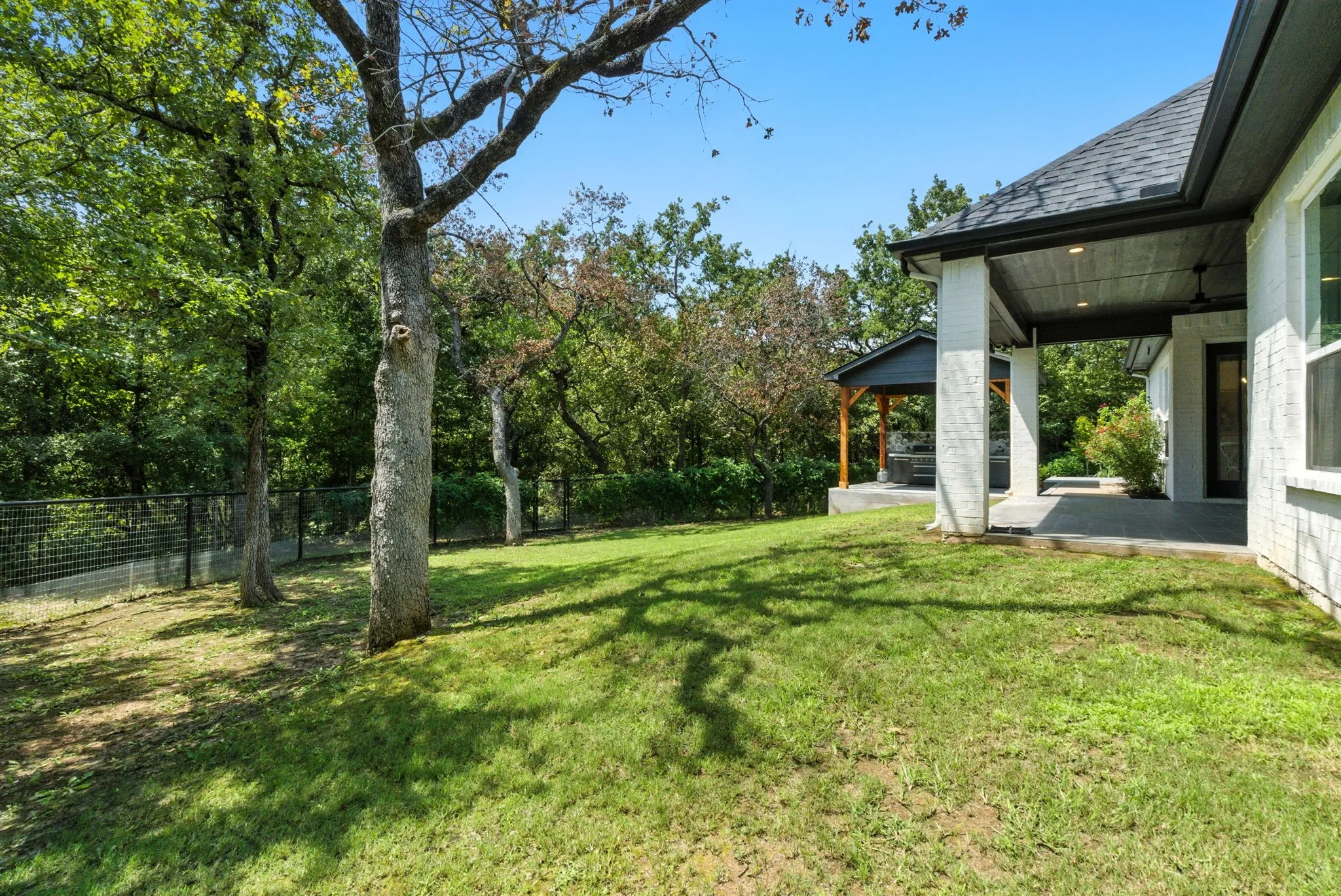 Expansive grassy yard with mature trees, a covered patio with recessed lighting, and a separate covered outdoor structure