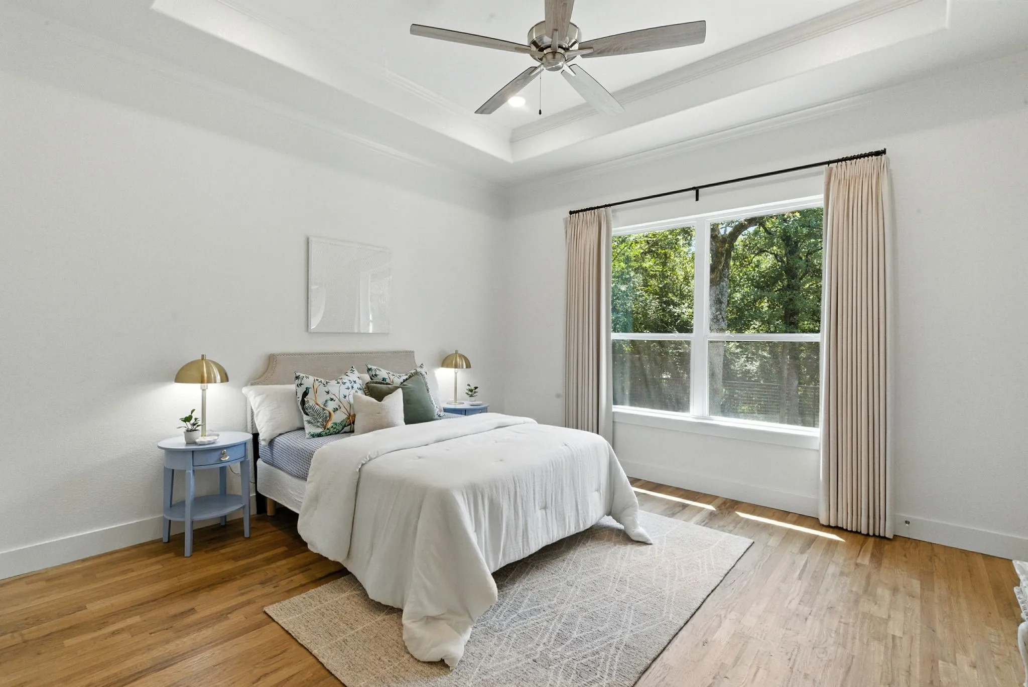 Tray ceiling with a ceiling fan, wood-finish flooring, and a large window with white trim
