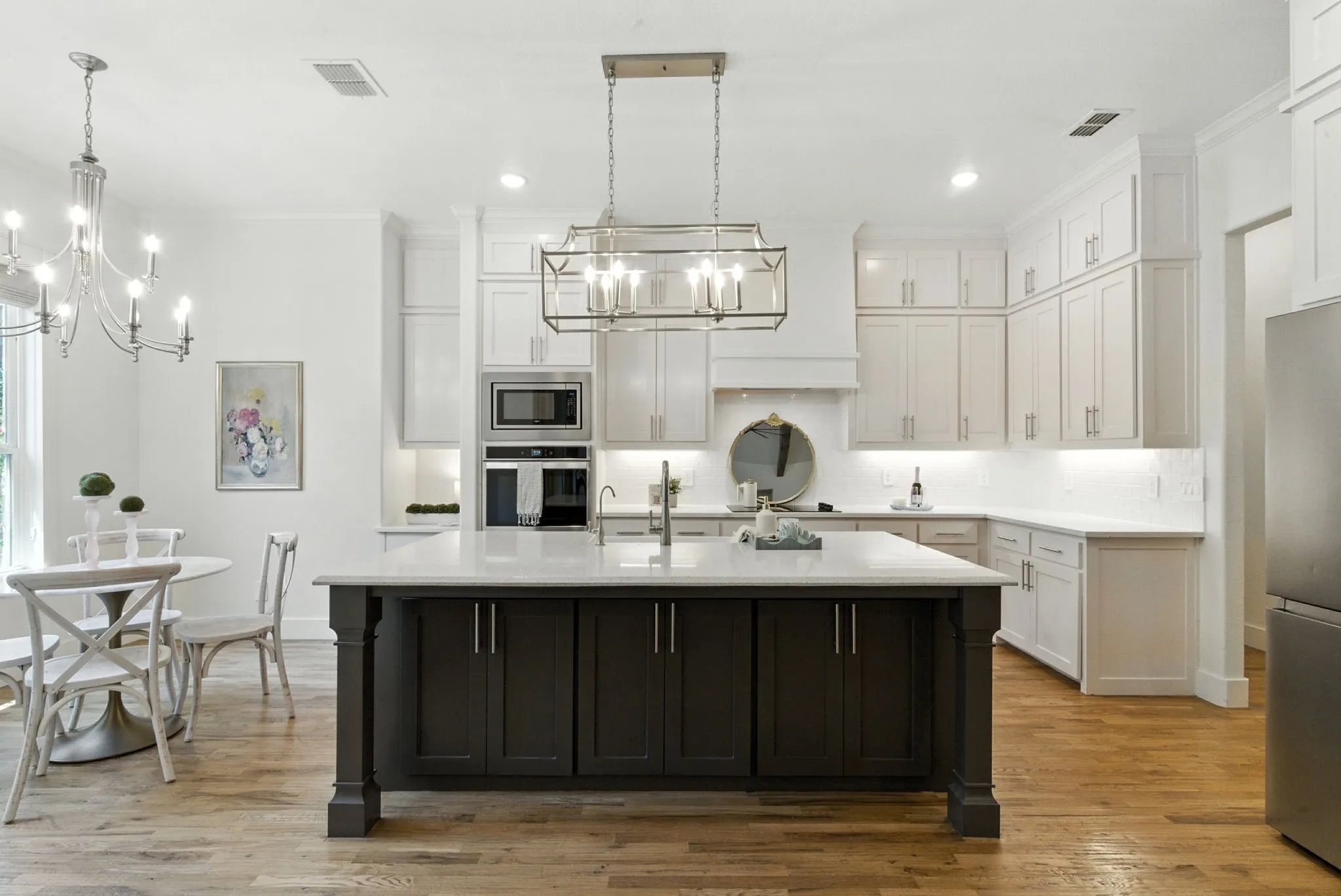 Expansive kitchen featuring white cabinetry, a dark-toned island with a light-toned countertop, integrated stainless steel appliances, and wood-finish flooring