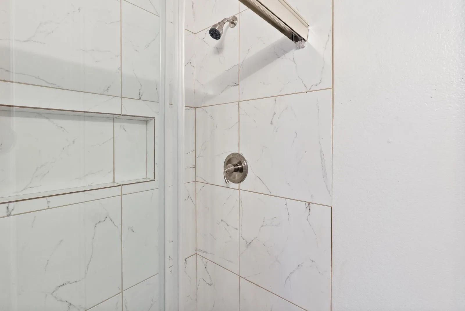 Tiled shower with a built-in niche, featuring a brushed nickel showerhead and control handle
