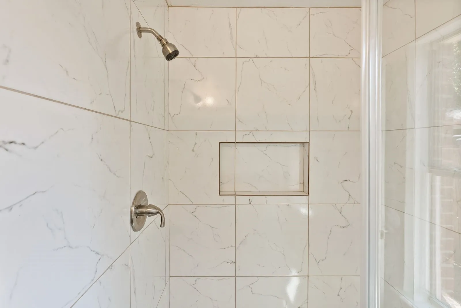 Shower with white tiled walls, a built-in niche, and brushed nickel fixtures