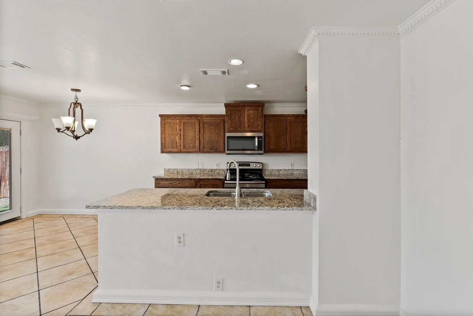 Kitchen featuring wood cabinetry, stainless steel microwave, and granite countertops