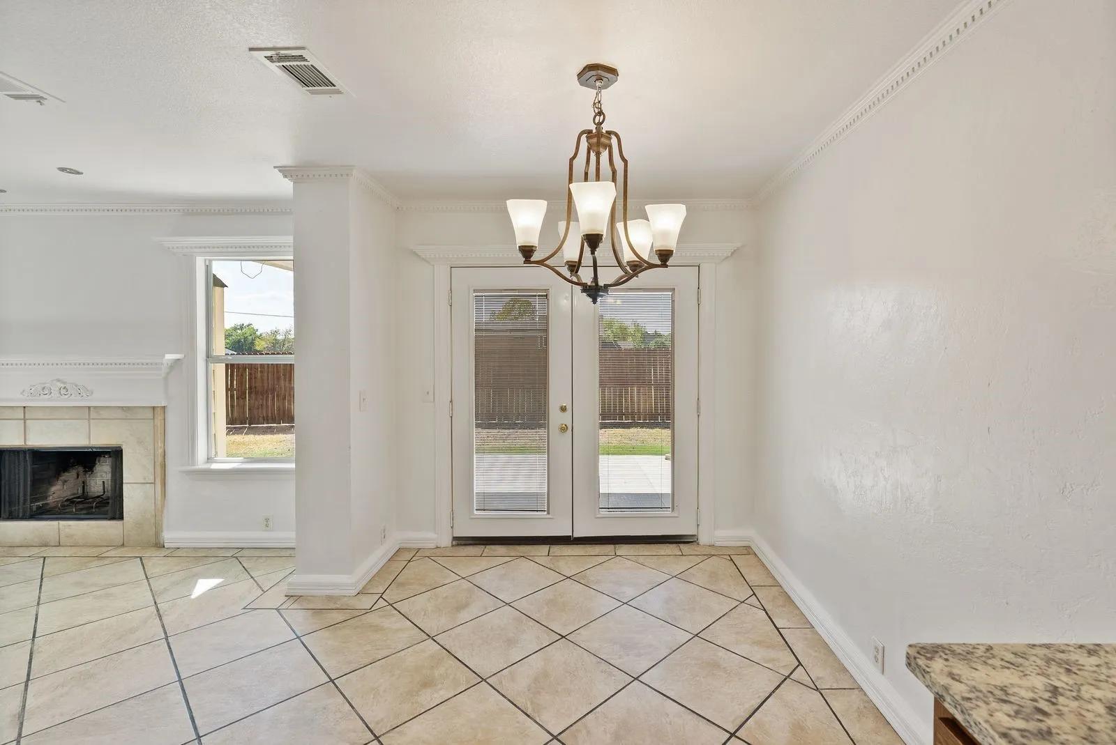Ceramic tile flooring, crown molding, built-in fireplace, double glass panel doors, and a decorative chandelier