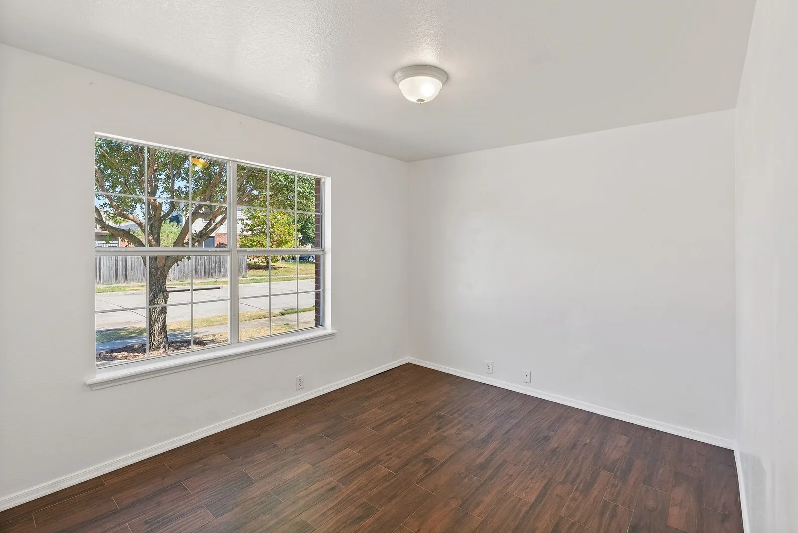 Wood-finish flooring, white walls, flush mount lighting, and a large window with white trim