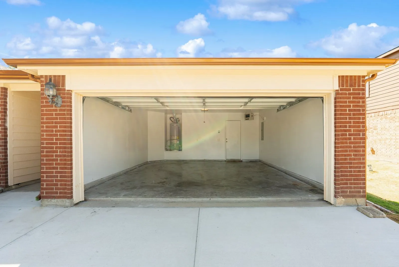 Two-car garage with brick veneer exterior, painted concrete floor, and exterior lighting fixture