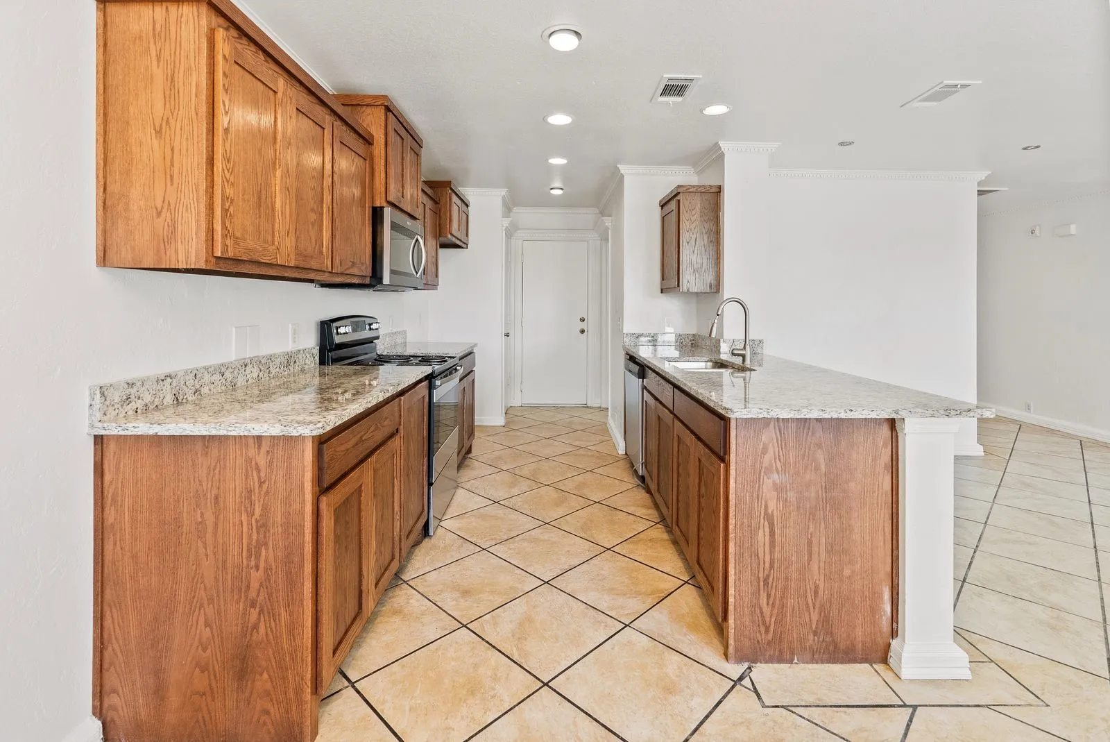 Kitchen featuring wood cabinetry, light-toned countertops, stainless steel appliances, and a diagonal tile flooring pattern