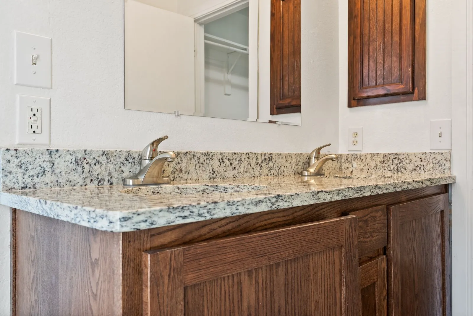 Dual vanity with stone-finish countertop, wood-finish cabinetry, and chrome fixtures