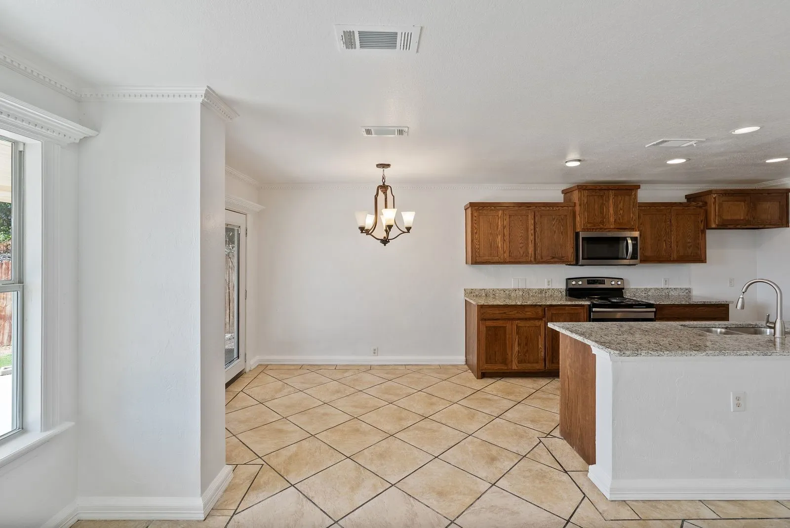 Open-concept area featuring diagonal tile flooring, a kitchen with wood cabinetry, granite countertops, and stainless steel appliances