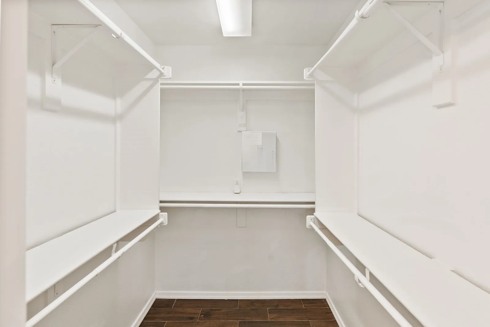 Walk-in closet with multiple white shelving units, integrated hanging rods, and wood-finish flooring