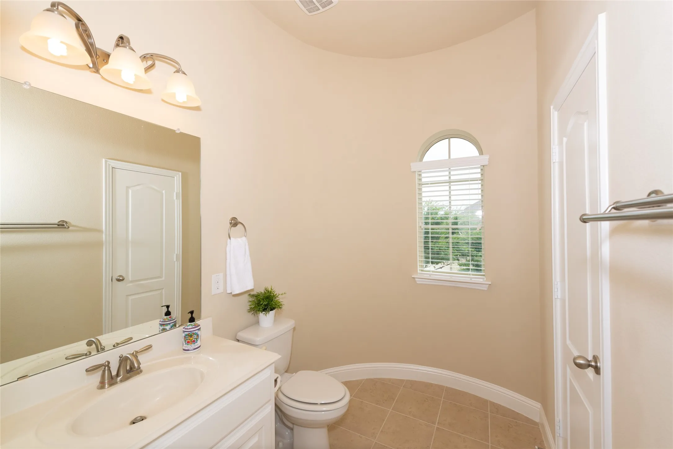 Vanity with integrated sink, arched window with horizontal blinds, tiled flooring, and a towel bar