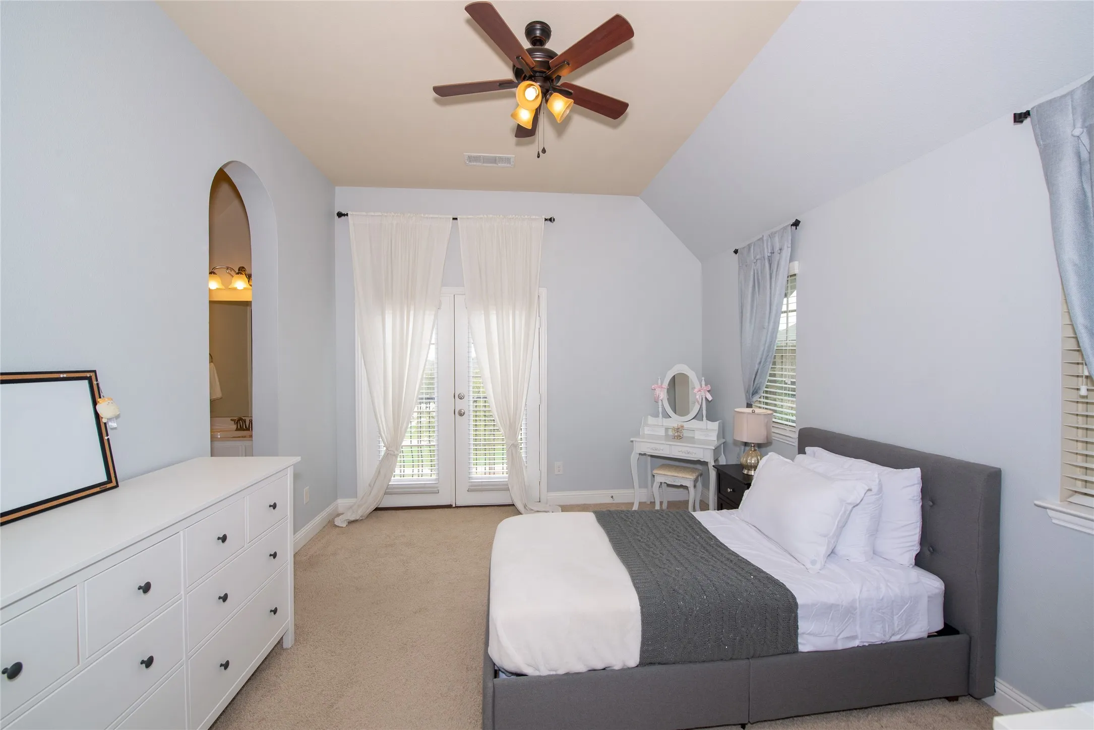 Vaulted ceiling with wood-finish ceiling fan, arched doorway, and double doors with blinds
