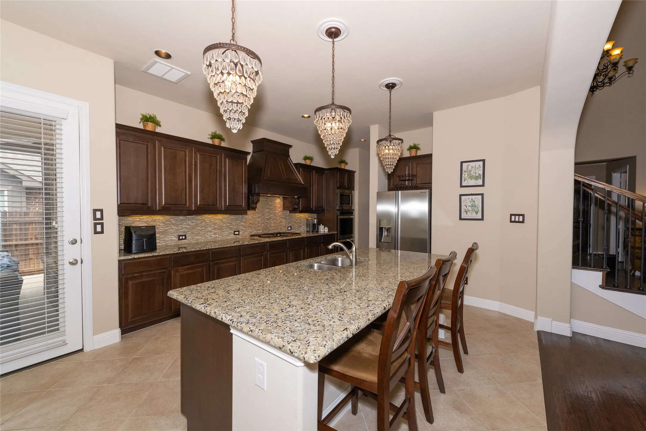 Kitchen featuring dark wood-finish cabinetry, a stone-finish island with integrated sink, stainless steel appliances, and decorative chandelier lighting