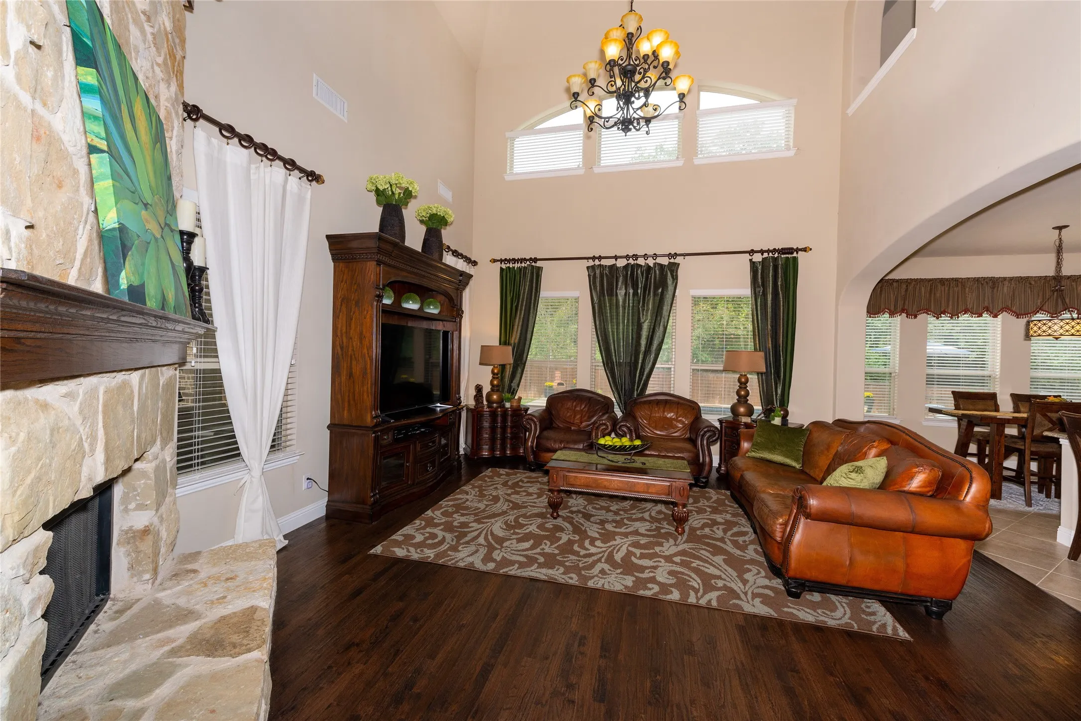 Vaulted ceiling with a chandelier, stone-faced fireplace, dark wood-finish flooring, and arched entryway