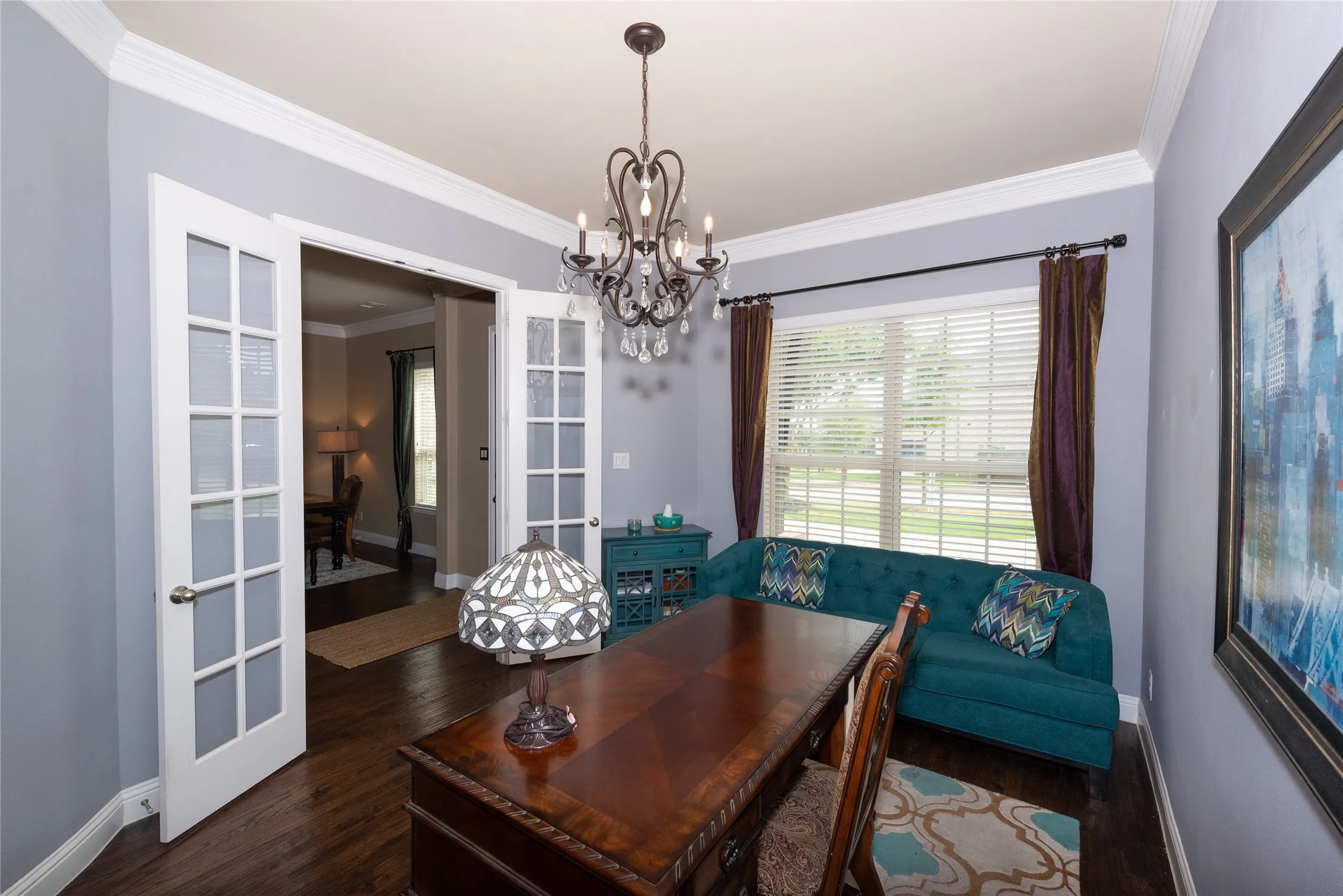 Elegant dining room featuring hardwood flooring, a decorative crystal chandelier, French doors with glass panes opening to additional living spaces, teal upholstered built-in banquette seating, and rich wood-finish dining table