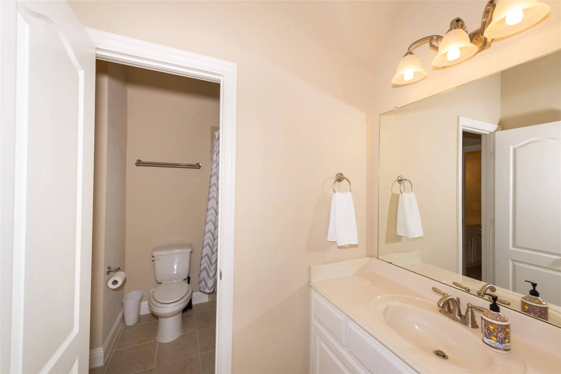 White vanity with an integrated sink, broad wall mirror, and brushed nickel light fixture
