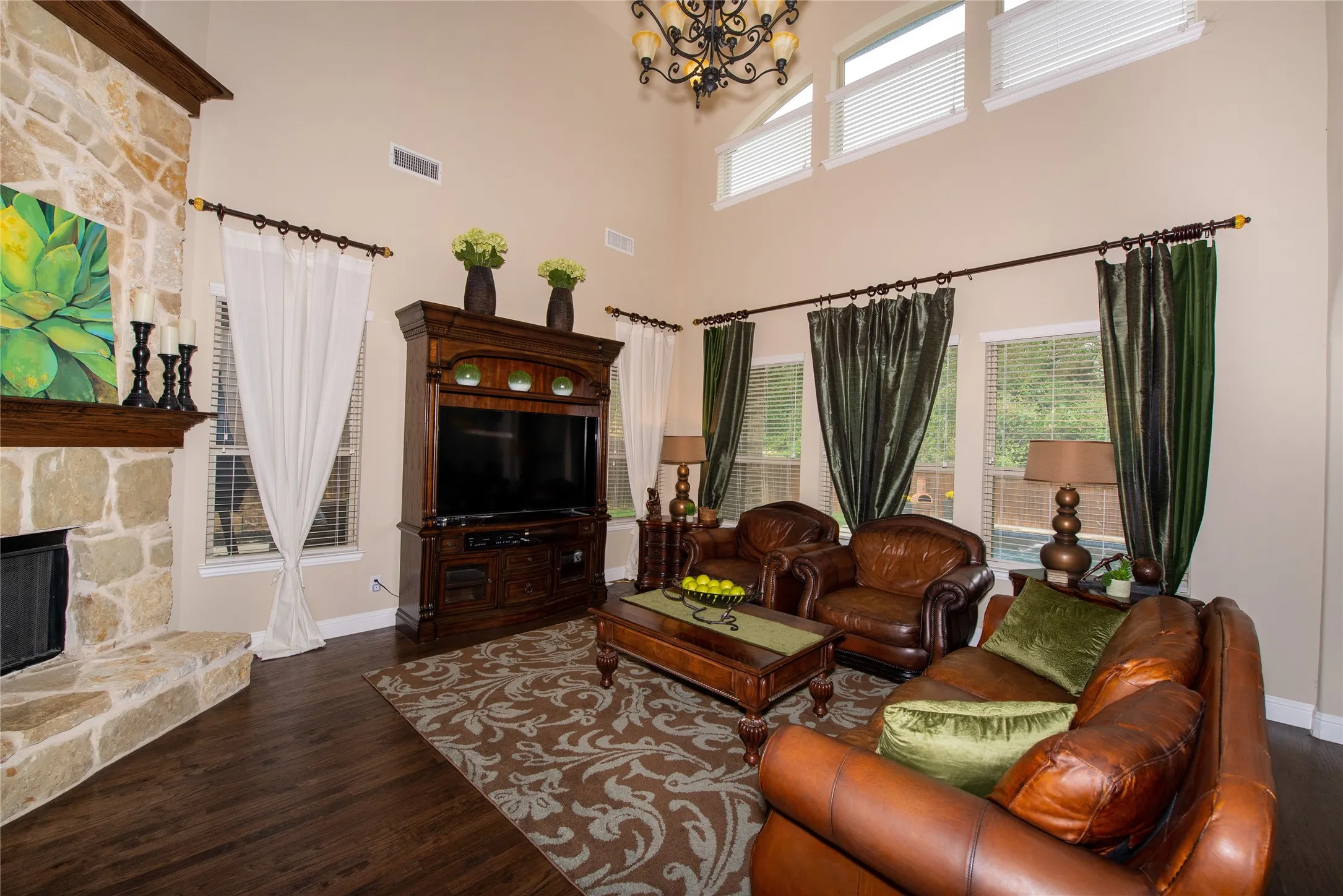 Living area featuring a stone fireplace with wood mantel, high ceilings, wood-finish flooring, and upper transom windows