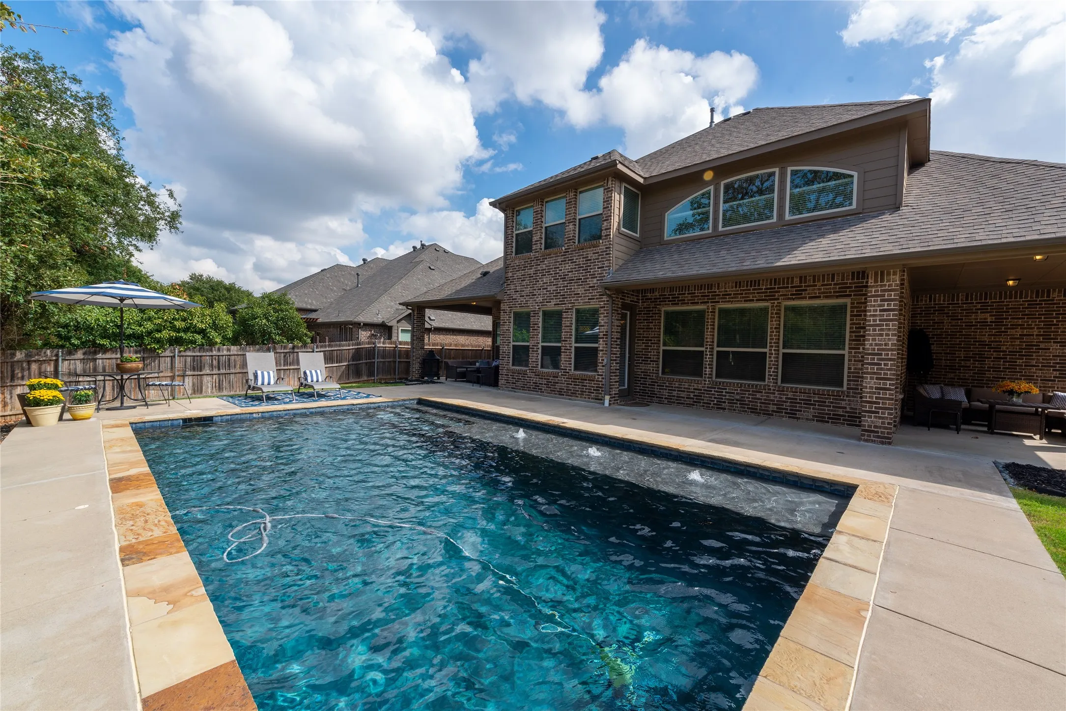 Brick exterior with a covered patio, an in-ground swimming pool, and a fenced backyard