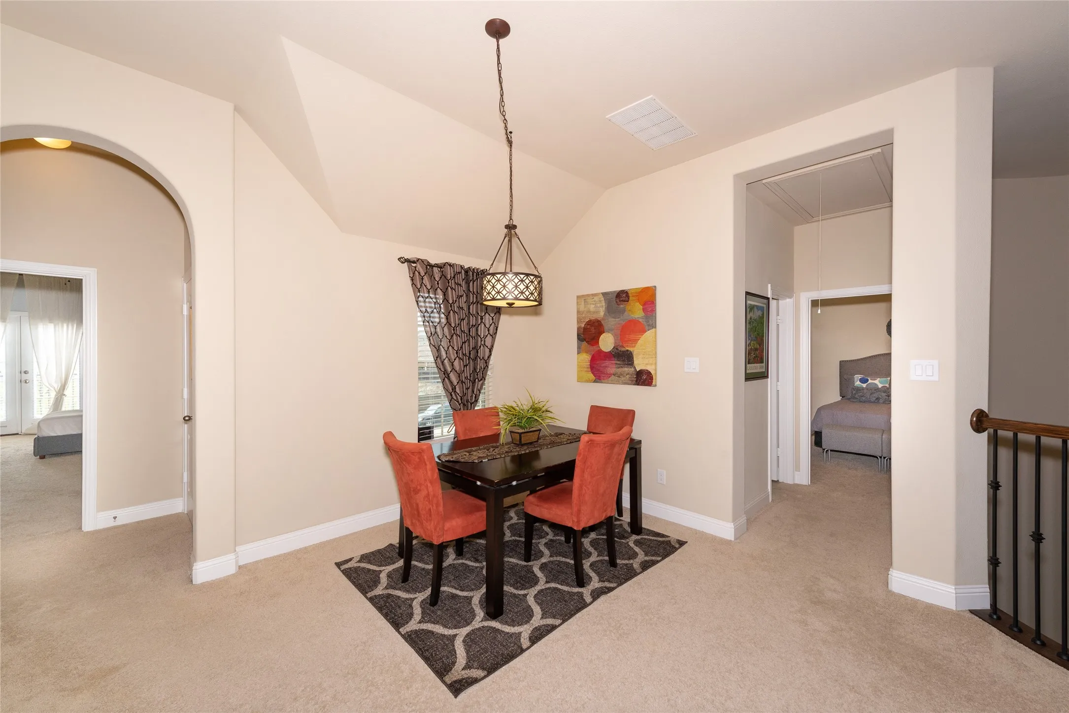 Sloped ceiling with recessed lighting, arched doorway, wrought iron railing, and a window with patterned drapes
