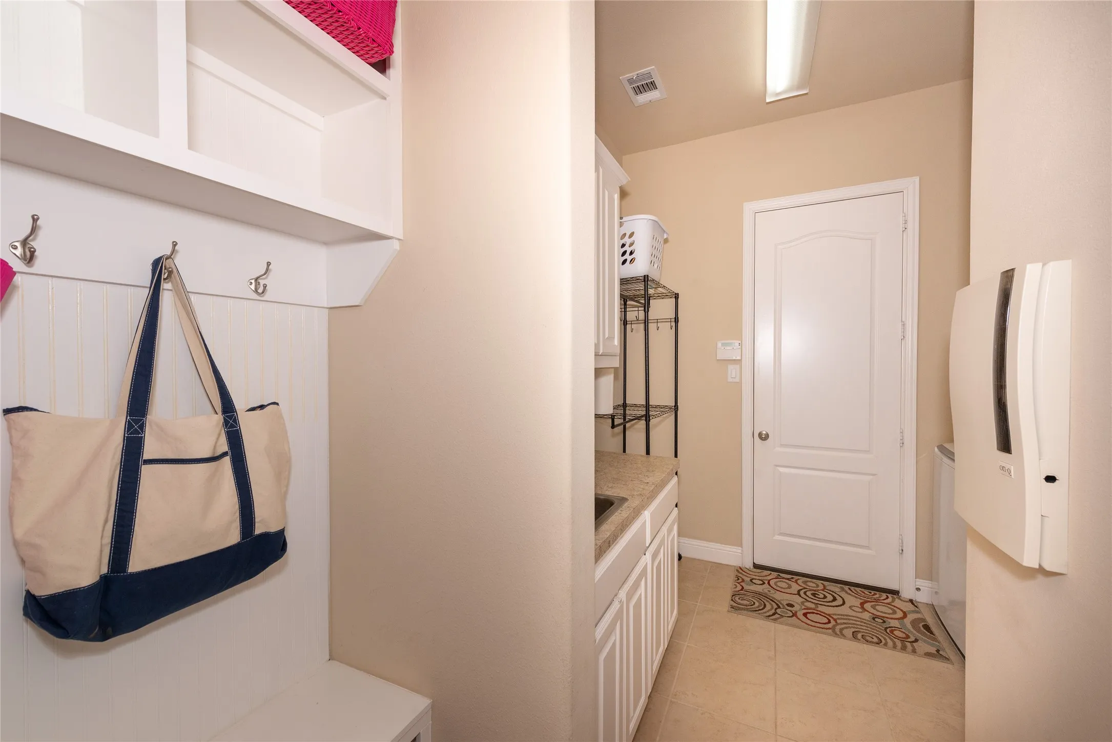 Built-in white storage cubbies with hooks, light-toned wall paint, ceramic tile flooring, and white paneled door