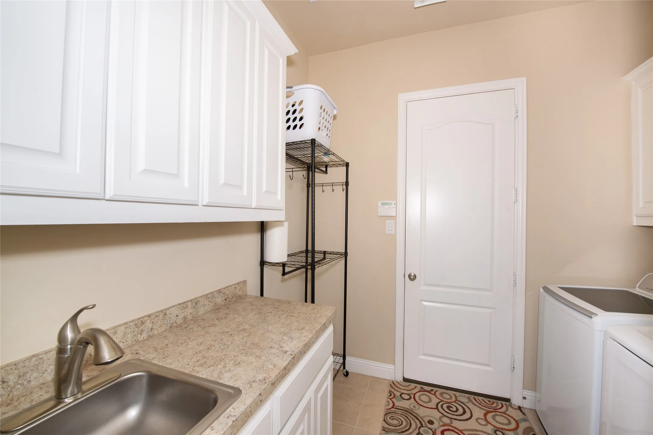 Utility room with upper and lower white cabinetry, a stainless steel sink, and light-toned countertop