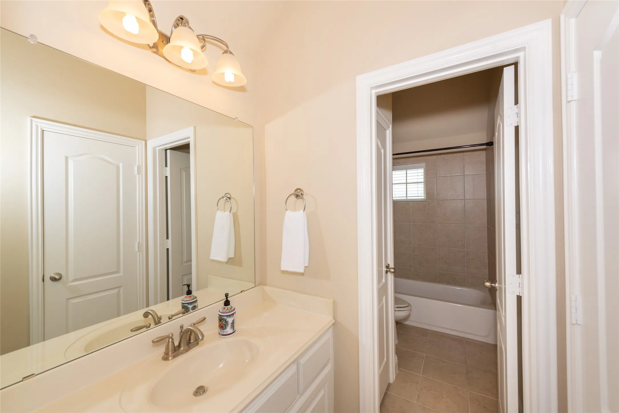 Master bathroom featuring a large framed mirror, dual vanity with white cabinetry and brushed nickel fixtures, ceramic tile countertop, recessed lighting, and an ensuite shower and tub combination with tile surround and glass enclosure