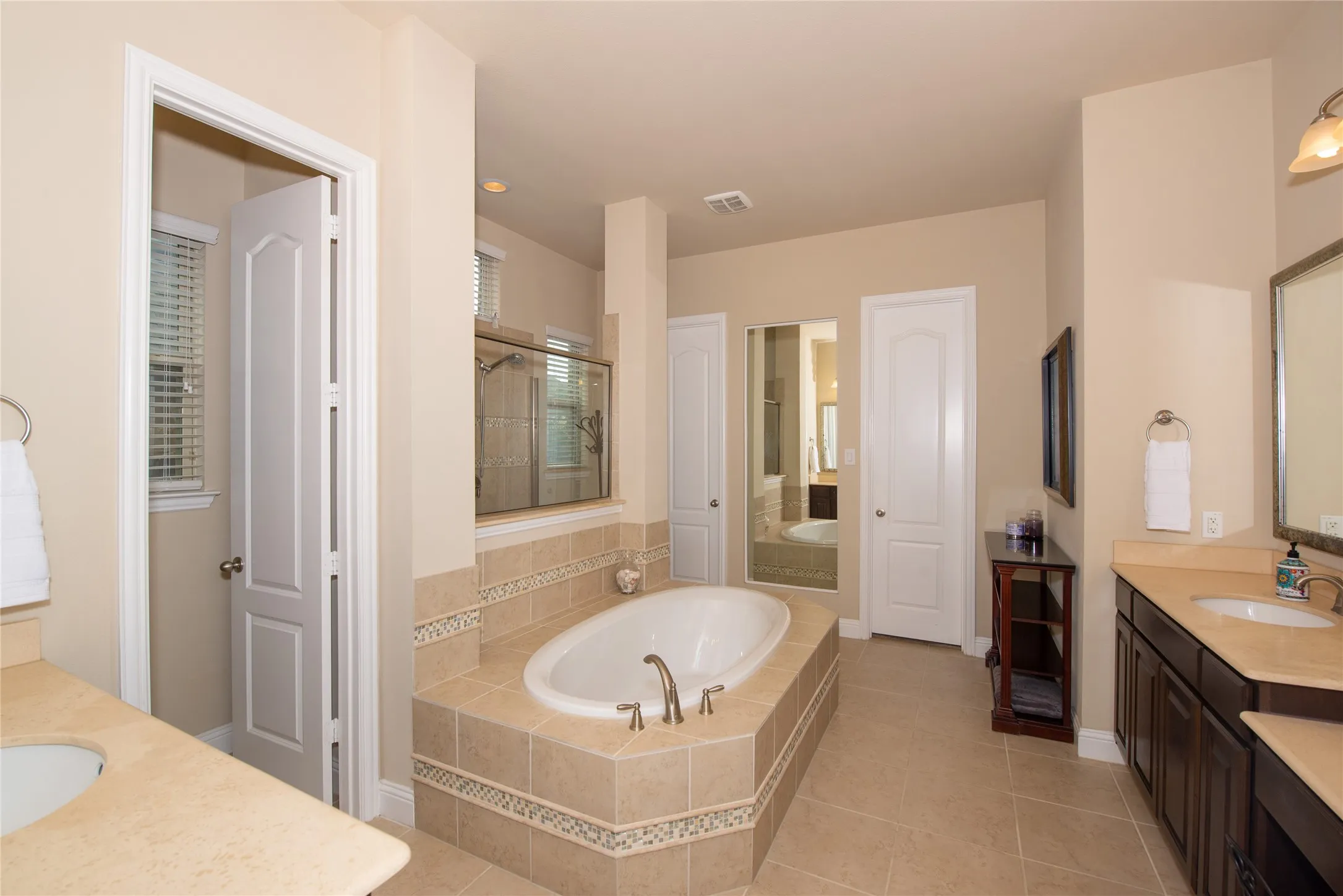 Tiled soaking tub, separate glass-enclosed shower, dual vanities with integrated sinks, and neutral-toned wall paint