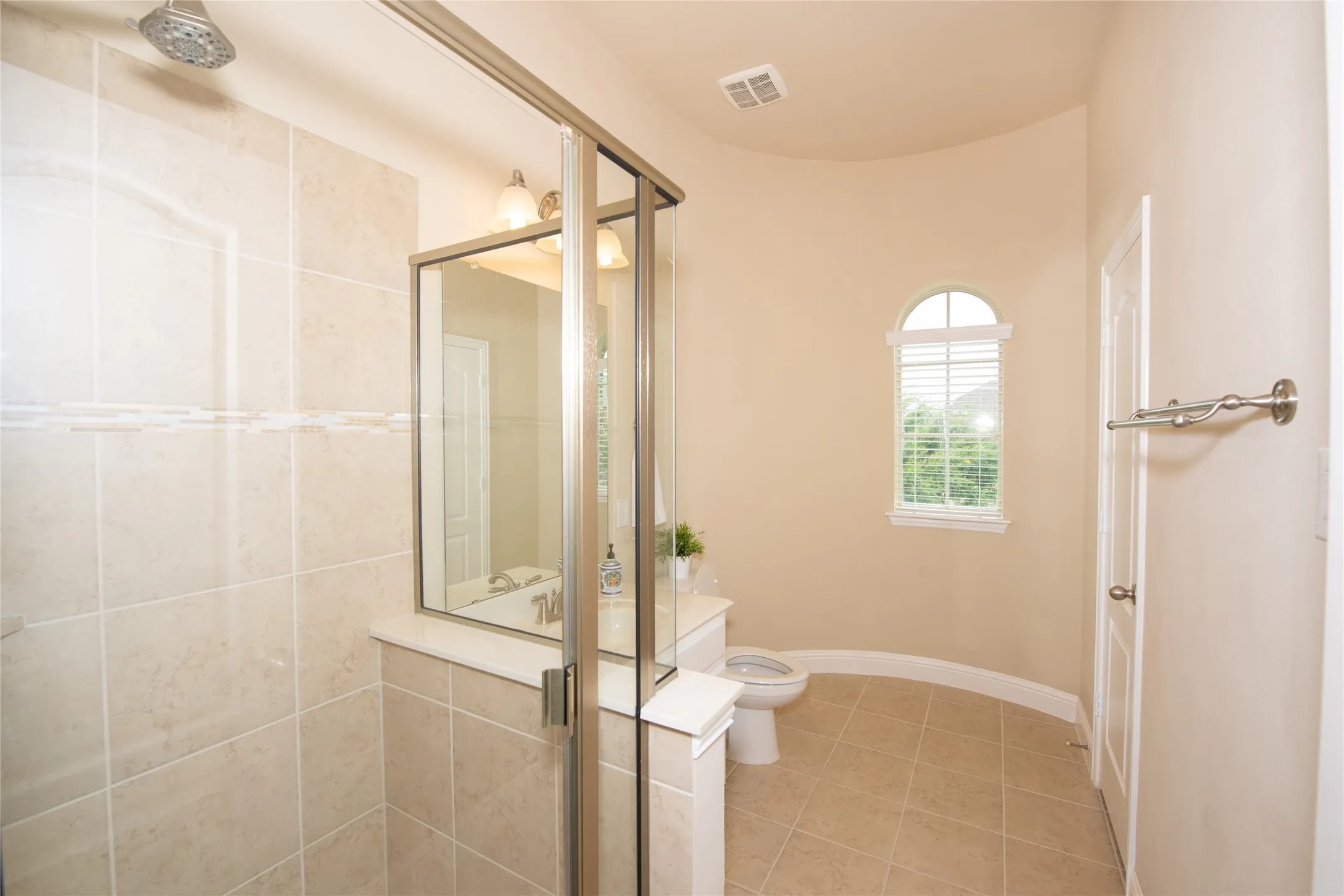 Tiled shower with glass enclosure, arched window with privacy blinds, and a vanity with an integrated sink