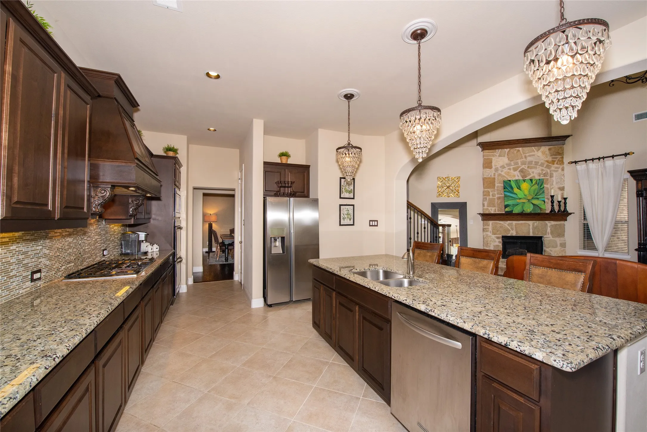 Kitchen featuring dark wood cabinetry, light-toned granite countertops, a built-in stainless steel dishwasher, and a stone fireplace surround with a​​‌​​​​‌​​‌‌​‌‌​​​‌‌​‌​‌​‌​​​‌​​ mantel