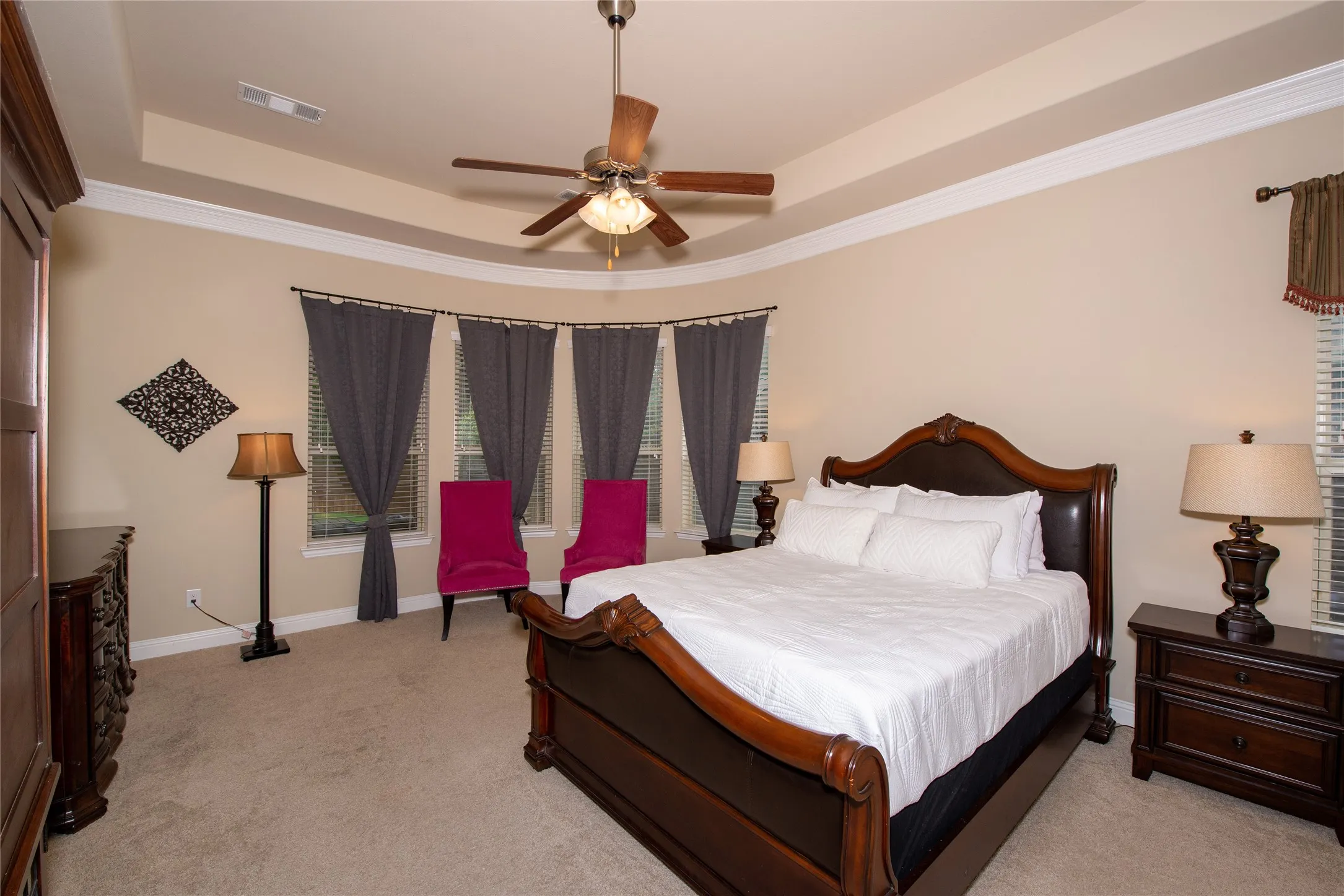 Tray ceiling with crown molding, ceiling fan with integrated lighting, multiple windows with blinds, and neutral carpeting