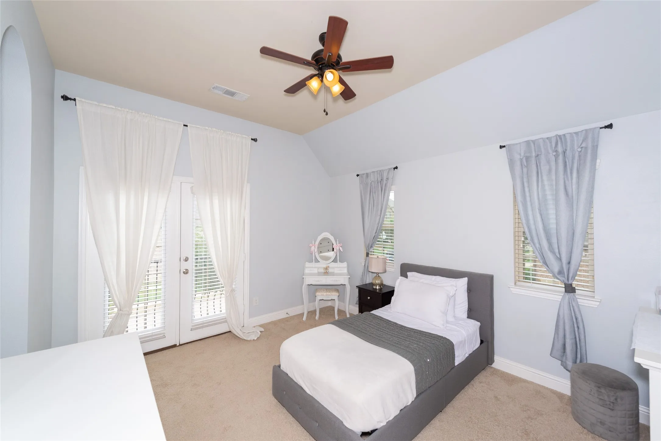 Vaulted ceiling with a ceiling fan, dual French doors, two windows, and neutral carpeting