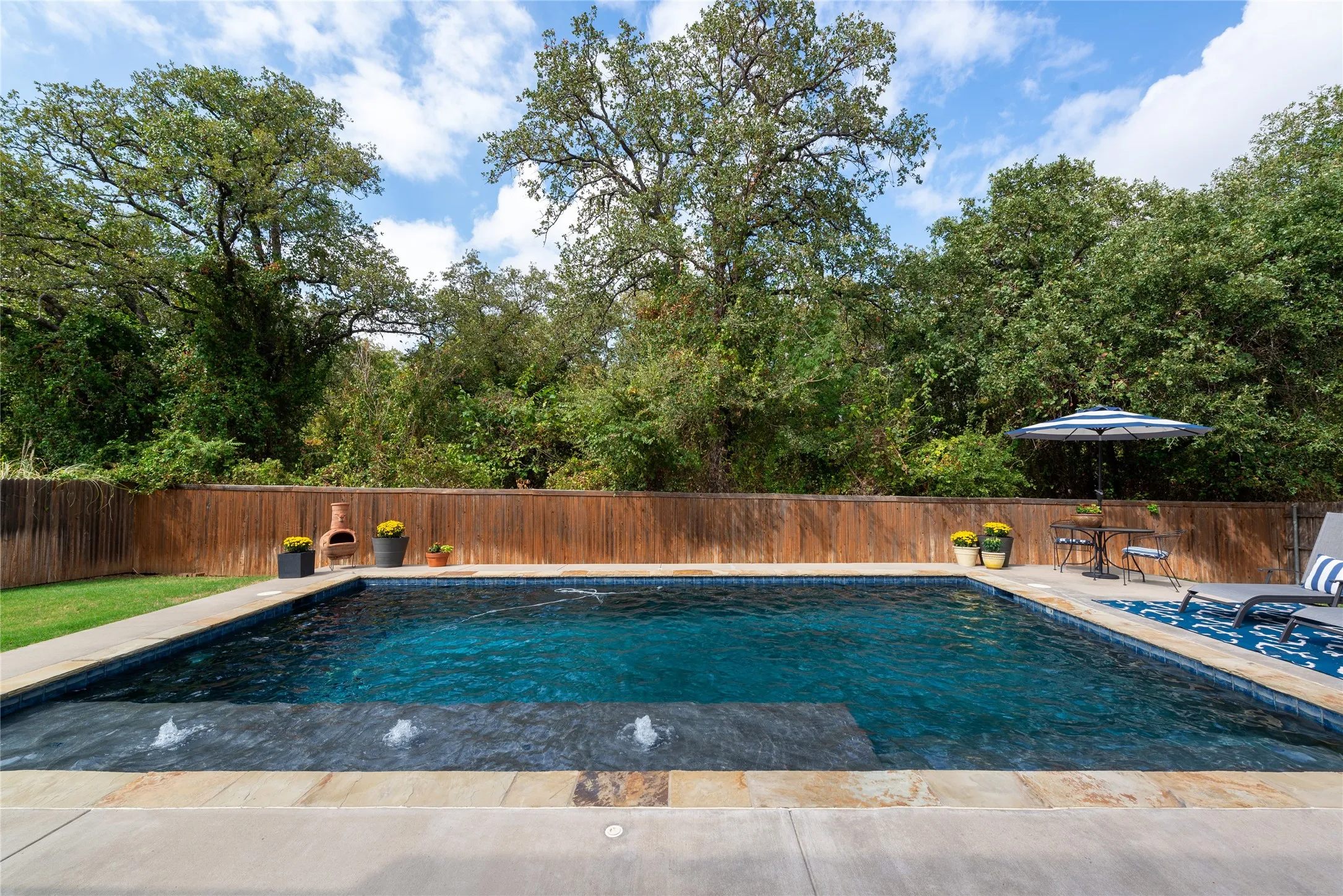 Rectangular swimming pool with integrated water features, stone coping, and a surrounding concrete patio